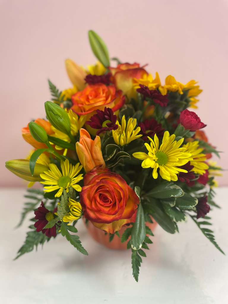Mixed bouquet of orange roses, yellow daisies, and lilies in a vase