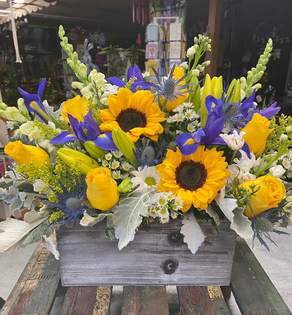 Mixed bouquet with sunflowers, yellow roses, and blue irises in a wooden box