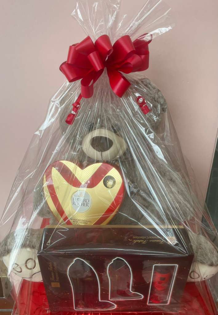 Gift basket with a teddy bear and heart-shaped chocolate box wrapped in clear plastic