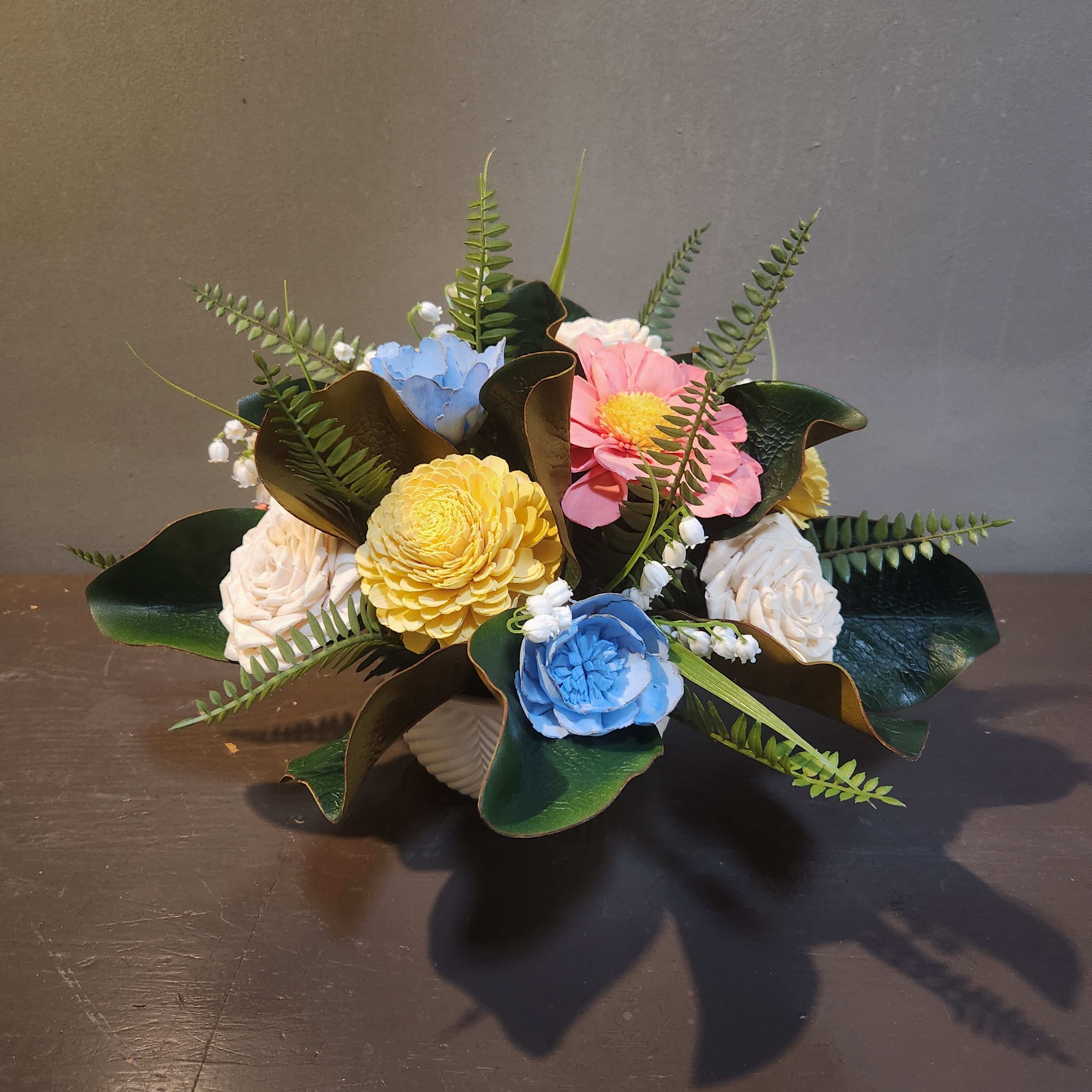 Small bouquet of pastel flowers with dark green leaves in a low container