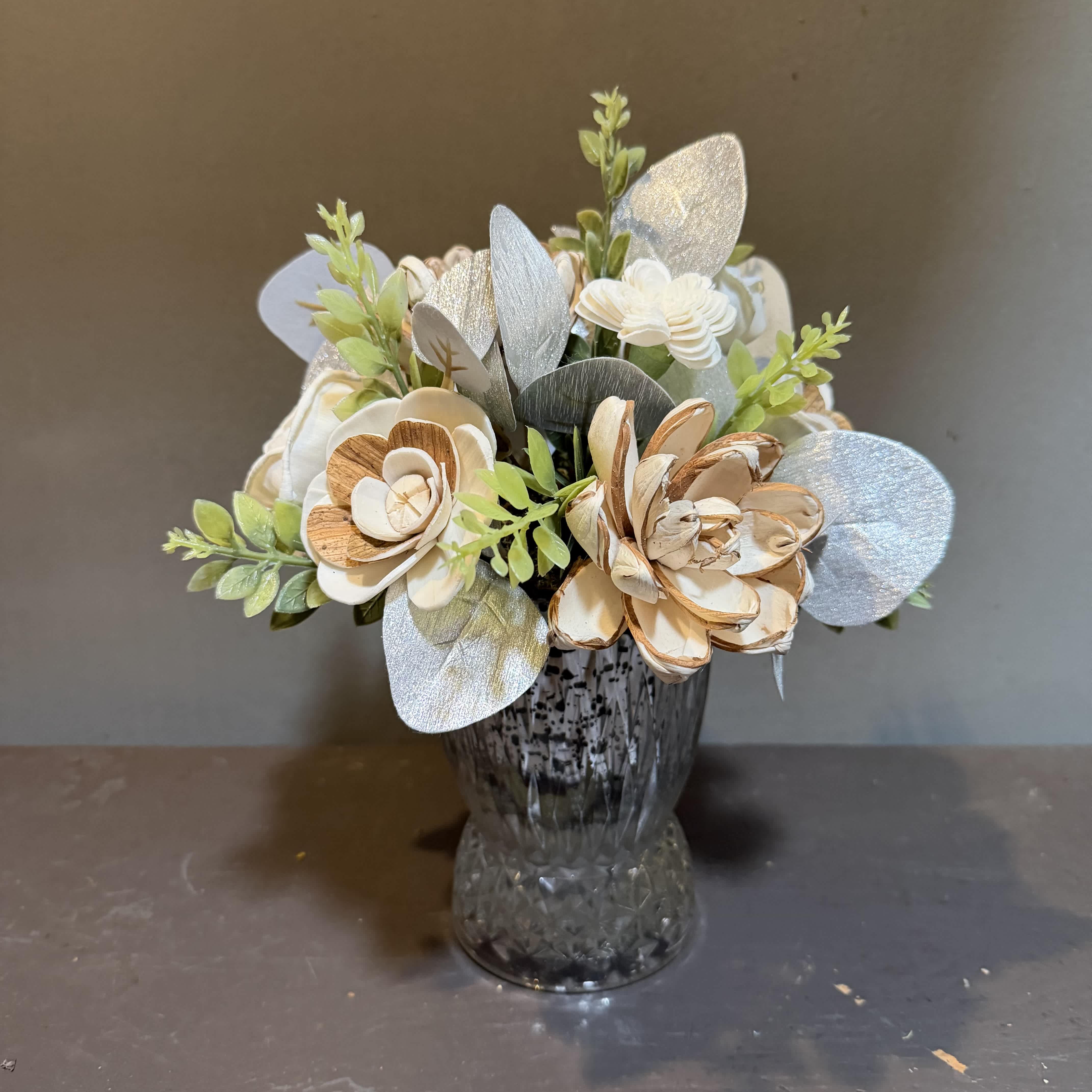 Artificial floral arrangement in a glass vase with silver and cream flowers