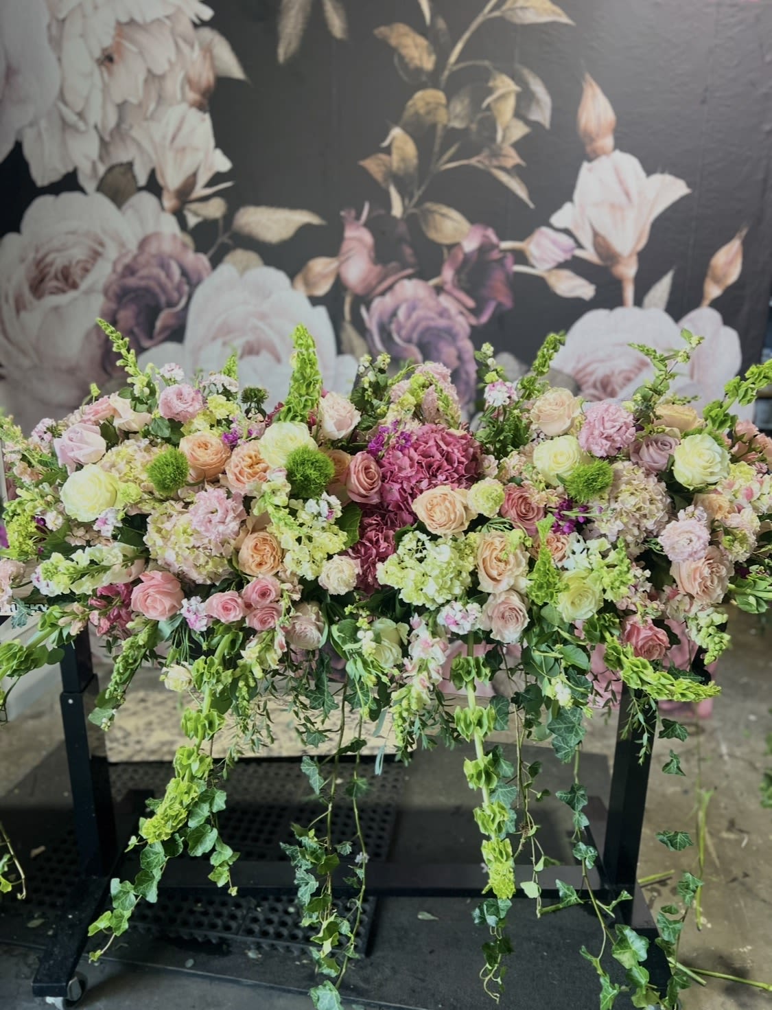 Large pastel floral arrangement with cascading greenery on a black stand