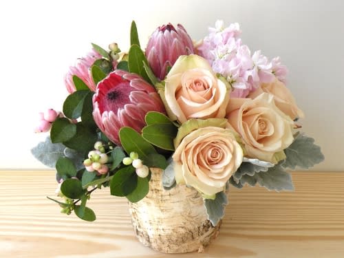 Bouquet of pale roses and pink protea in a birch bark container