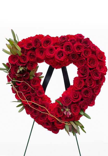 Heart-shaped red rose wreath on a stand with small greenery accents