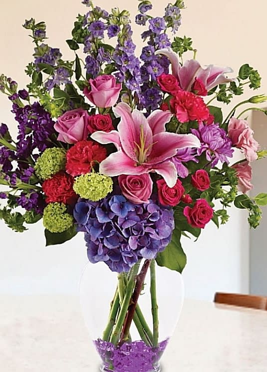 Mixed bouquet of pink roses, lilies, and purple flowers in a clear vase
