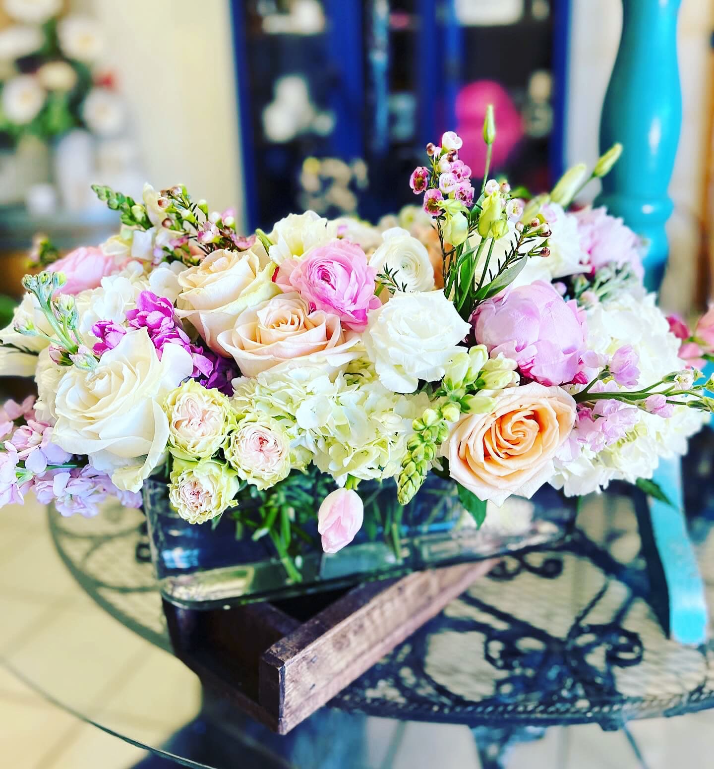 Pastel bouquet of roses, ranunculus, and small pink blooms in a low container