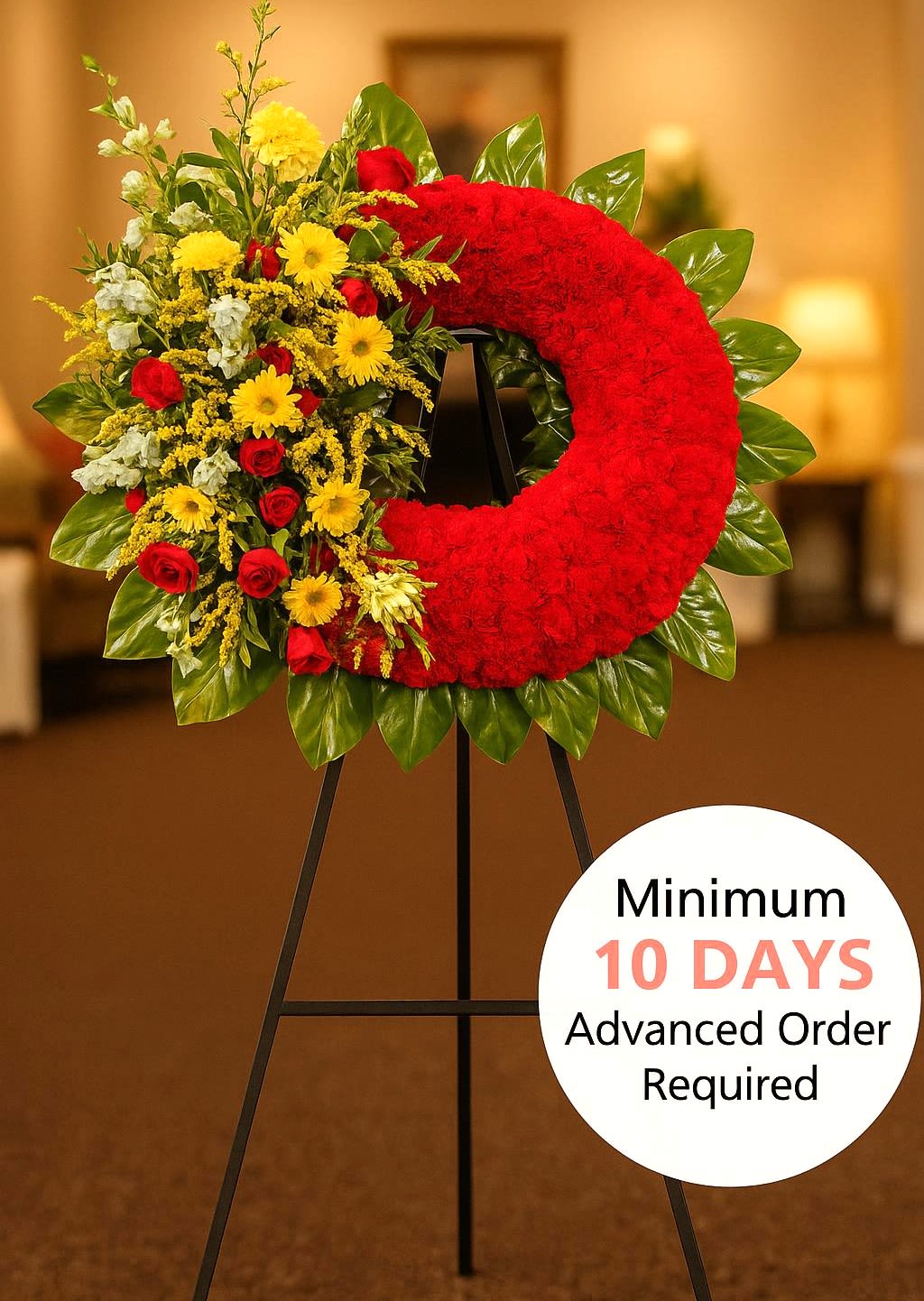 Standing red wreath with yellow and red flowers on one side, displayed on a black easel indoors