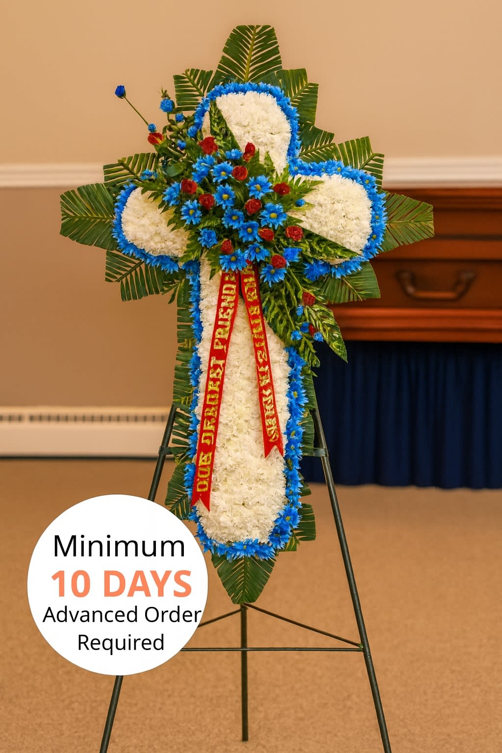 Standing cross-shaped funeral spray of white flowers with blue and red accents on an easel