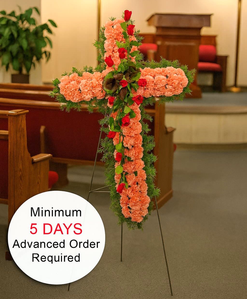 Tall peach carnation cross with red roses and greenery on an easel in a church