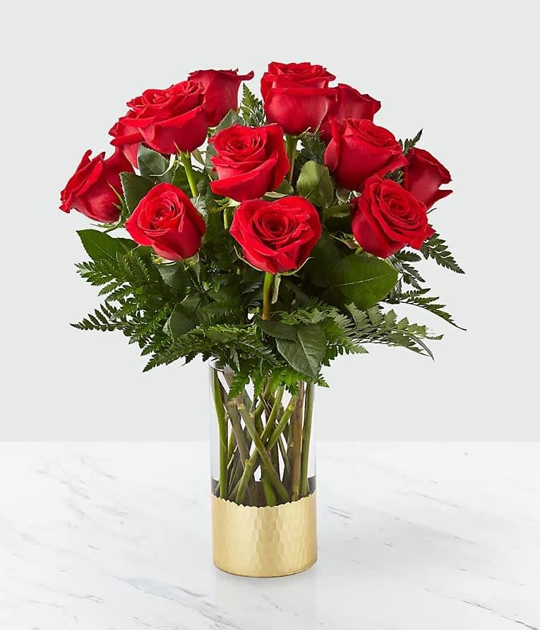 Red roses arranged in a clear glass vase with a gold base