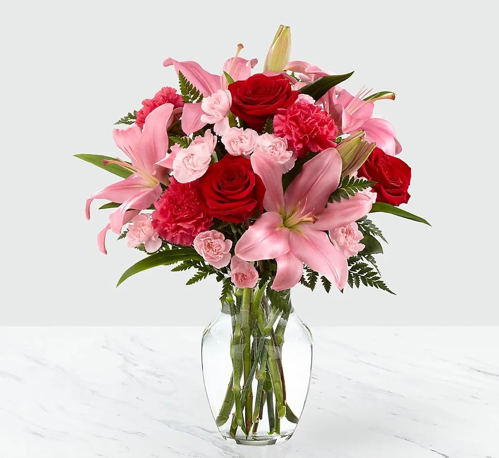 Pink lilies and red roses arranged in a clear glass vase