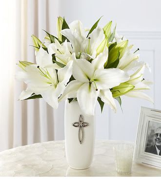White lilies arranged in a tall white vase with a cross emblem