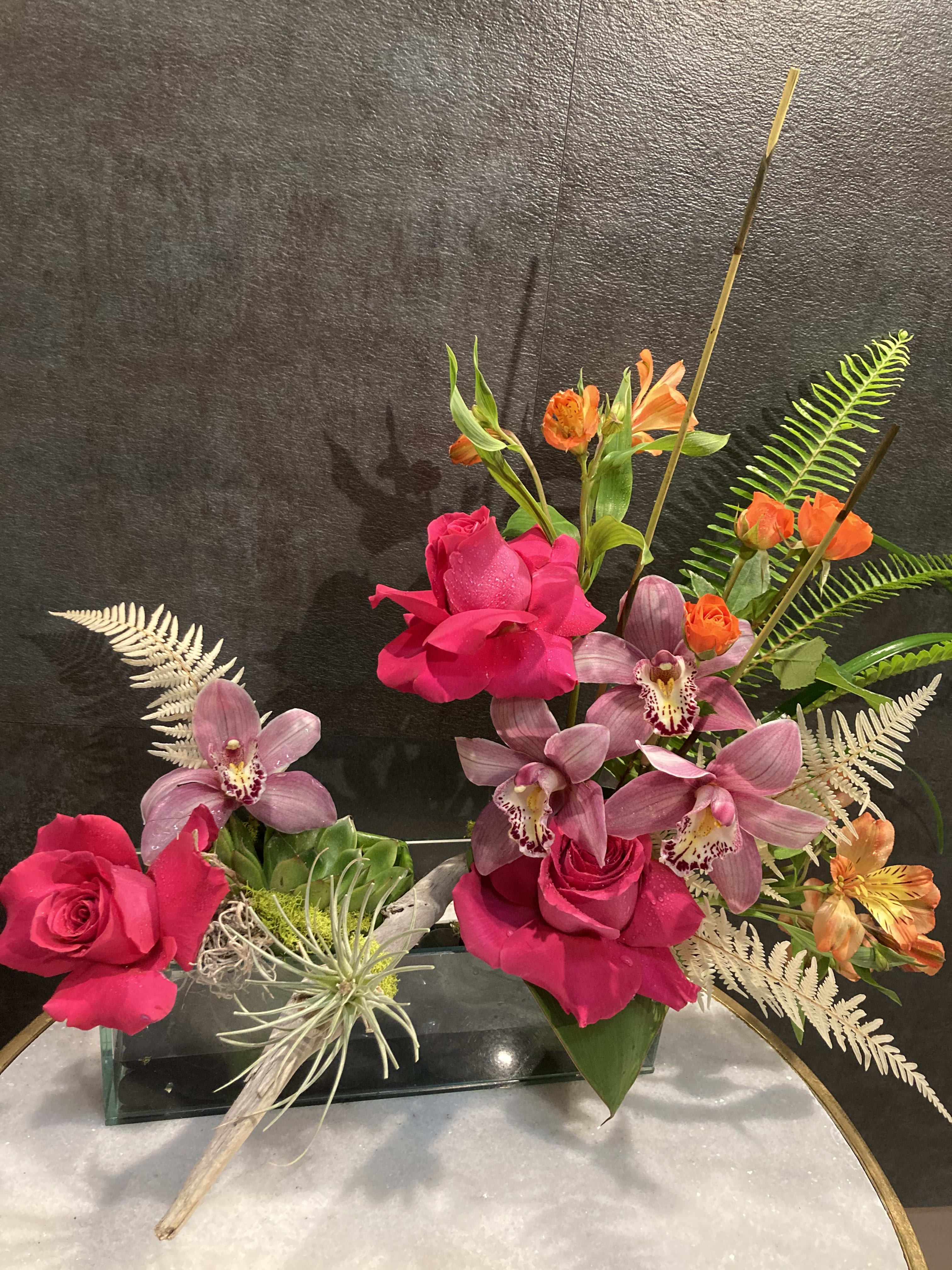 Pink roses and purple orchids arranged in a glass vase with orange accents