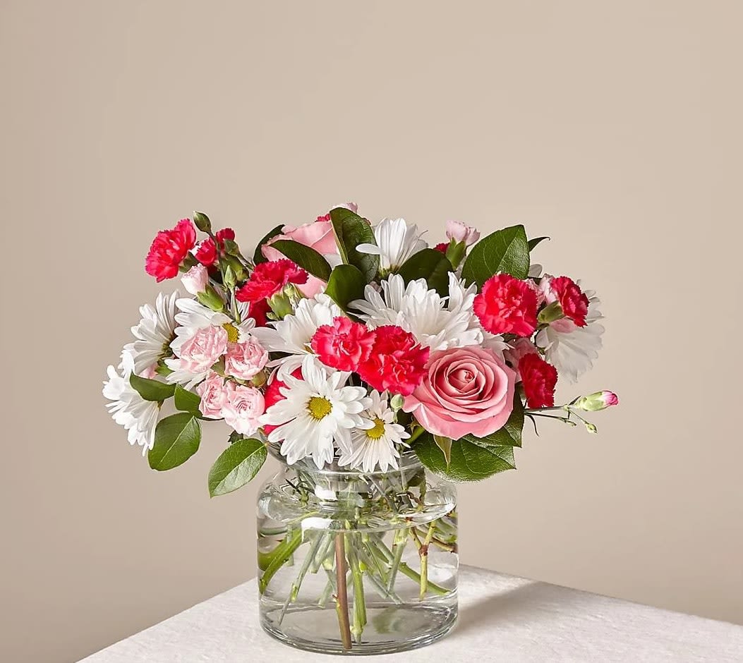 Pink roses, white daisies, and red carnations in a clear glass vase