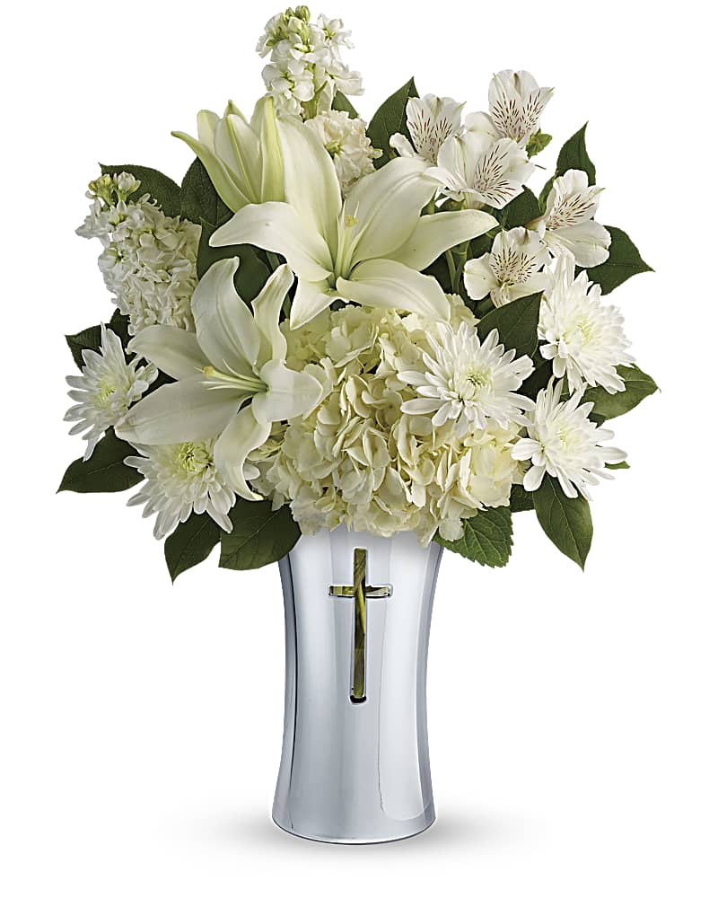 White lilies and daisies arranged in a silver vase with a cross cutout
