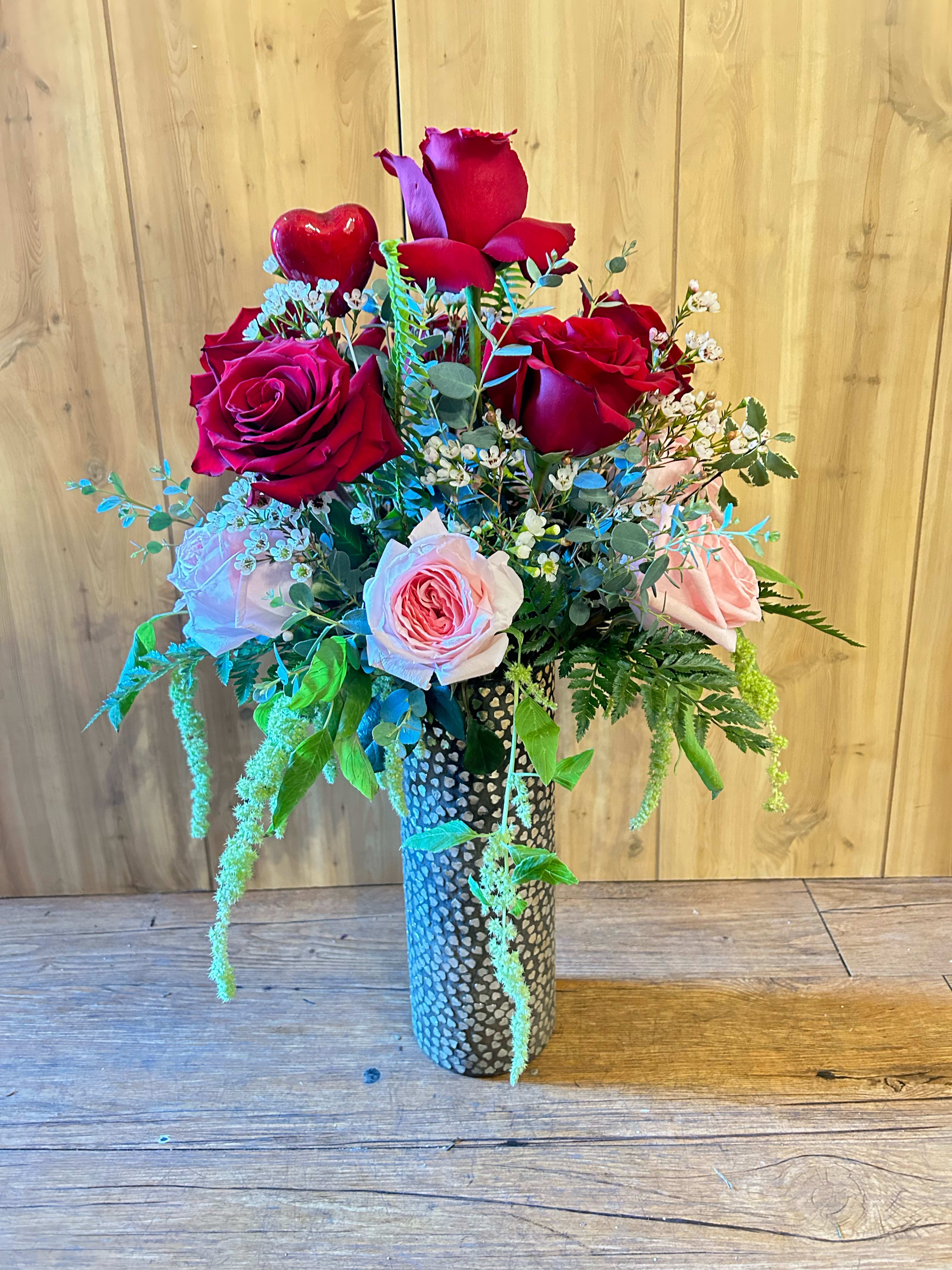 Bouquet of red and pink roses in a tall patterned vase with a heart accent