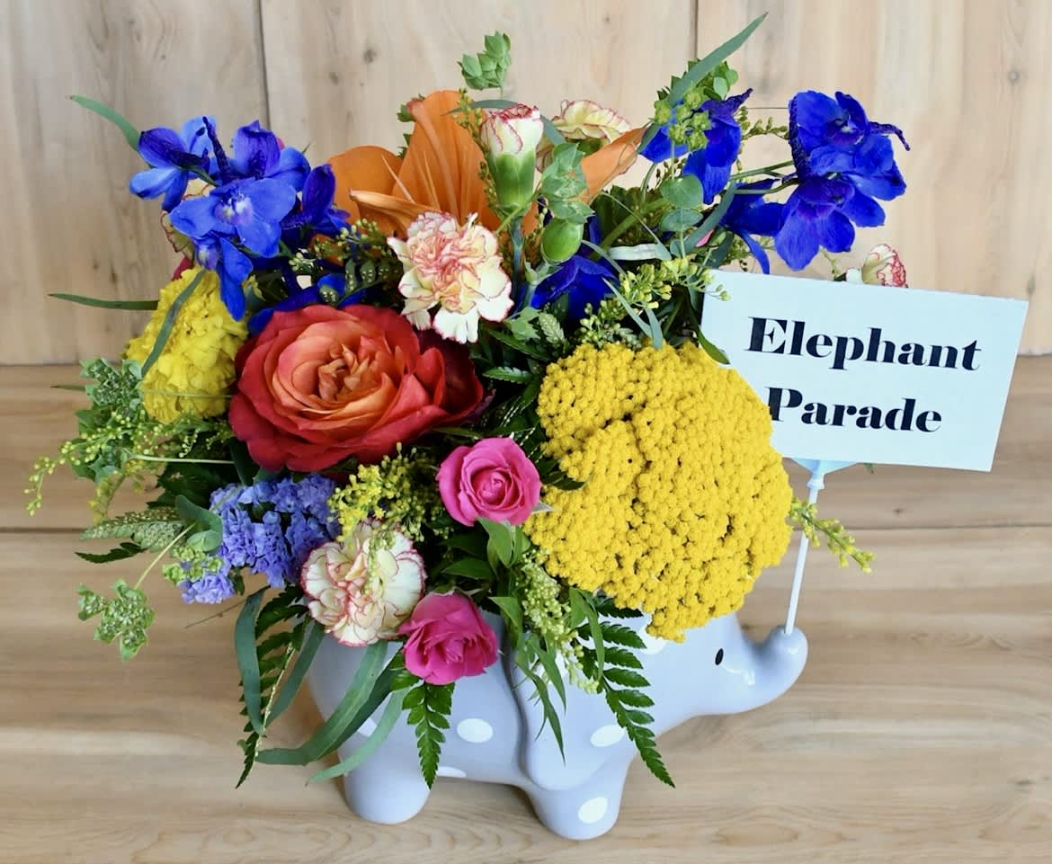 Colorful flower arrangement in a white elephant container with a sign reading Elephant Parade