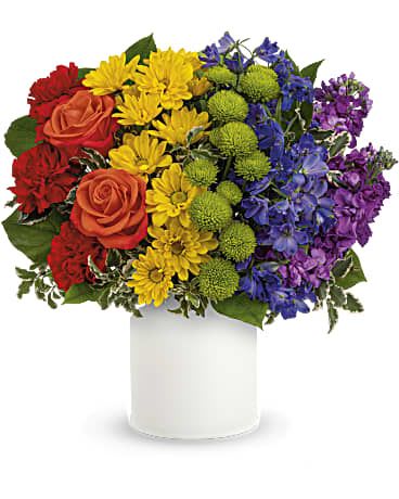 Rainbow bouquet of roses, daisies, and purple flowers in a white vase