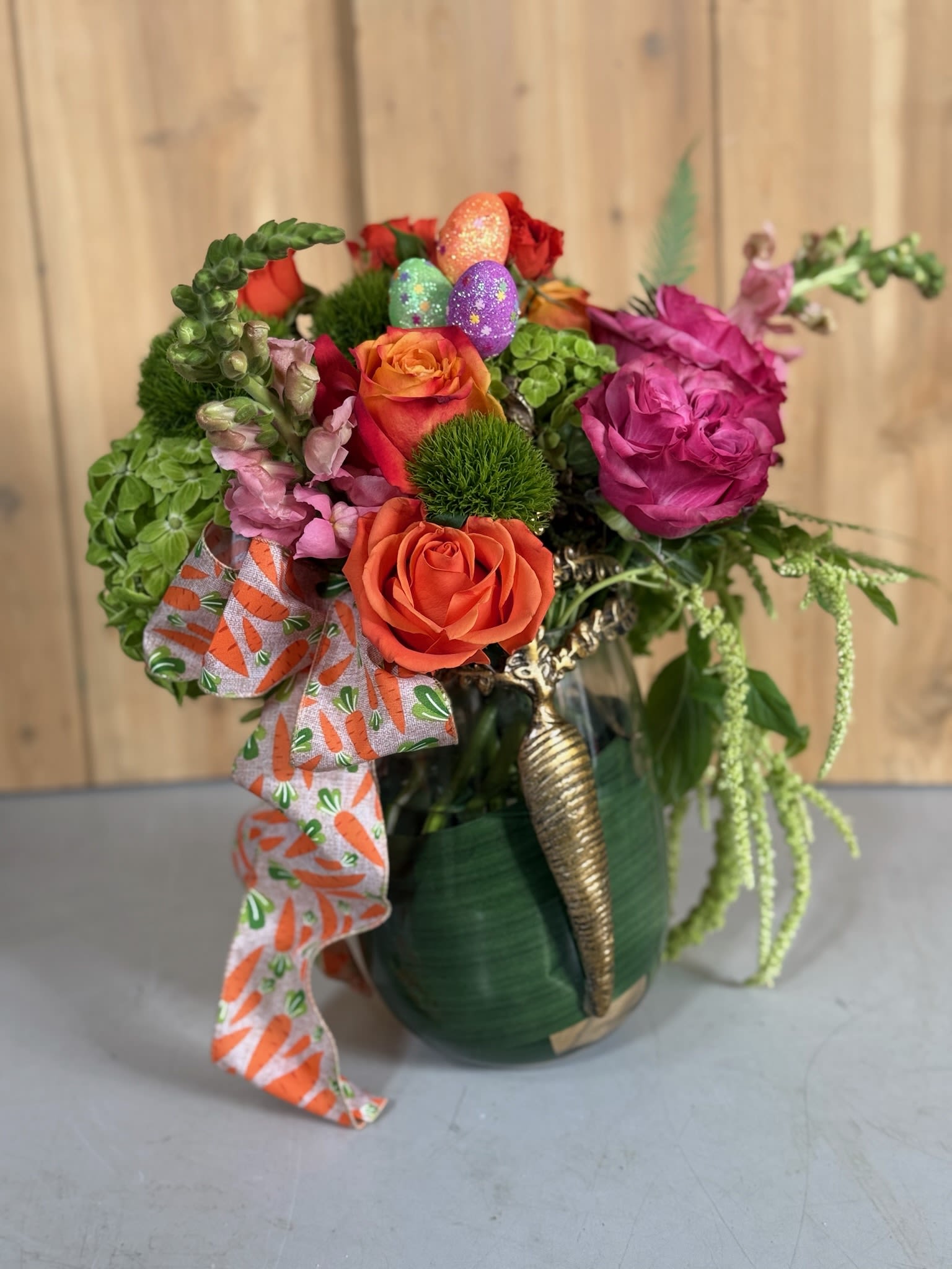 Colorful bouquet of roses and greenery in a green vase with a carrot-print ribbon