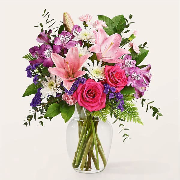 Mixed bouquet of pink lilies, roses, and purple flowers in a clear glass vase