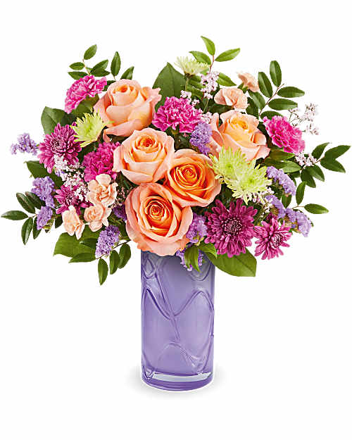 Peach roses and pink flowers in a purple glass vase