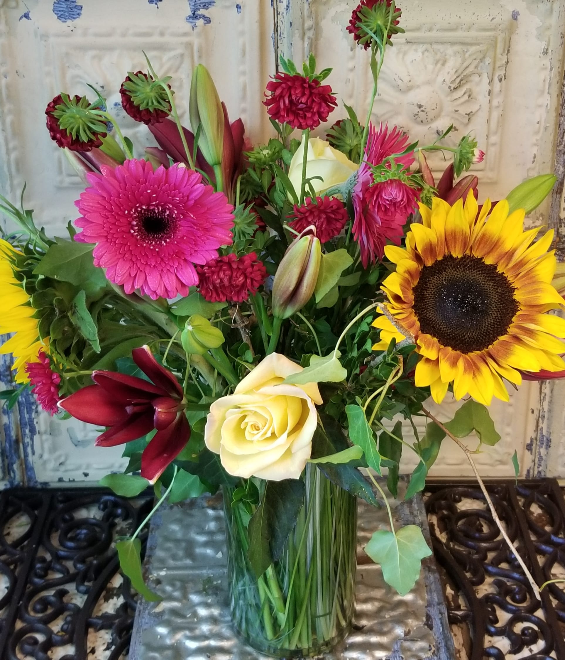 Mixed bouquet with sunflowers, roses, lilies, and pink gerbera daisies in a glass vase