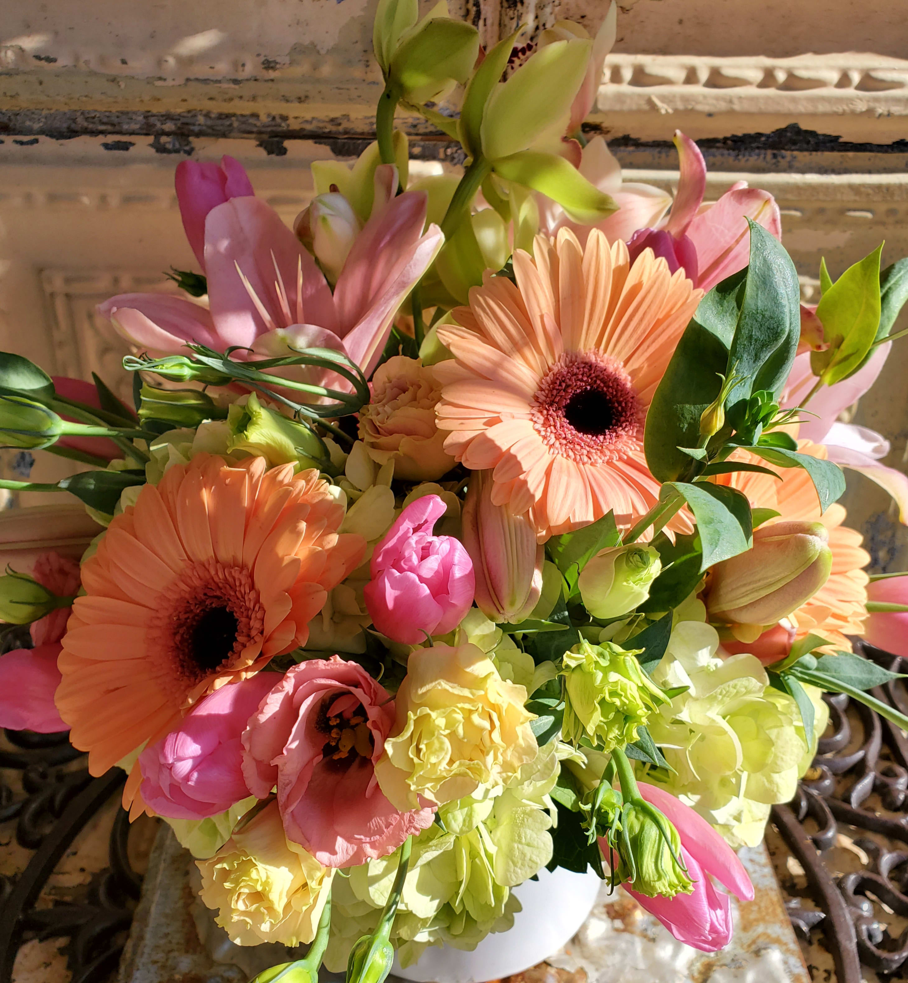 Bouquet of peach gerbera daisies, pink lilies, and pale green blooms in a white vase