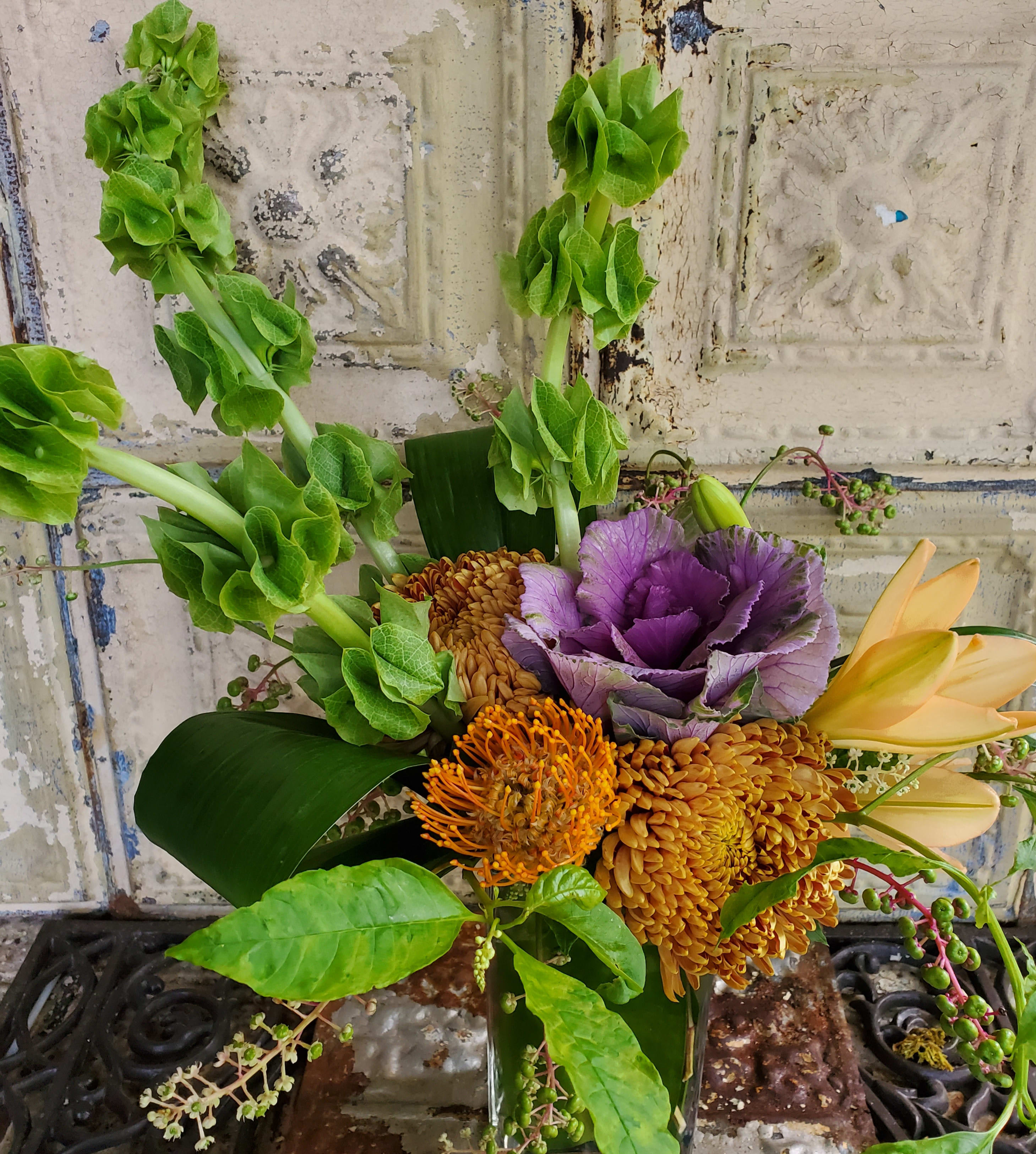 Bouquet with green bells of Ireland, purple cabbage, and orange blooms in a vase