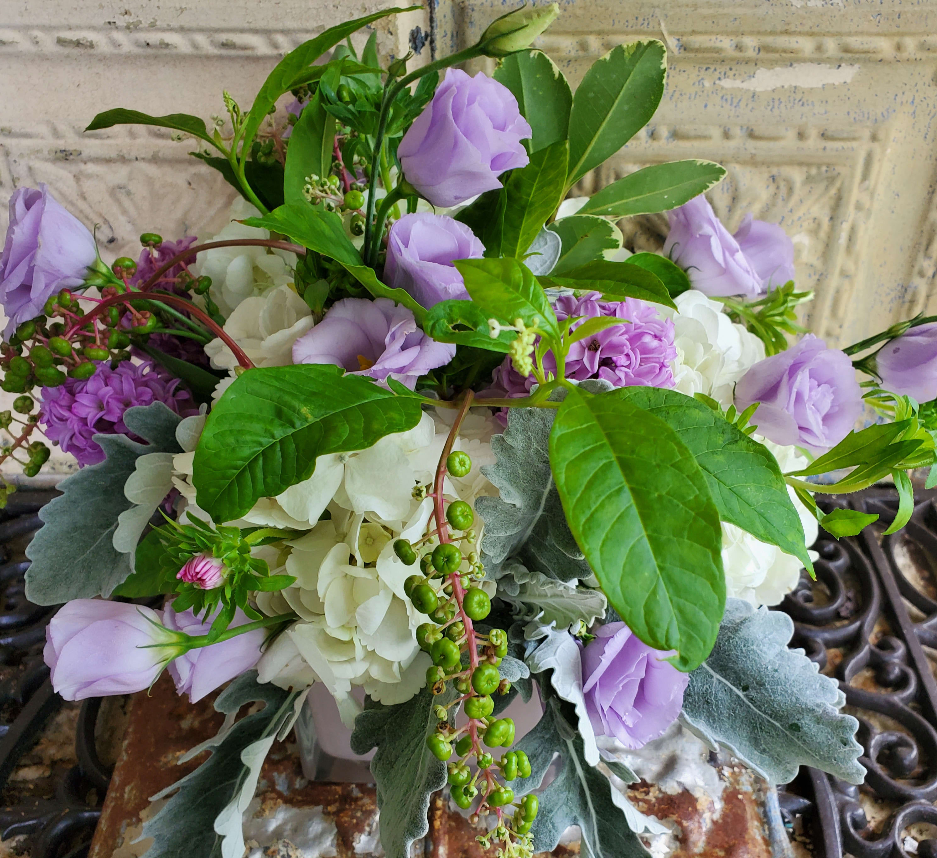 Lavender and white floral arrangement with greenery in a container
