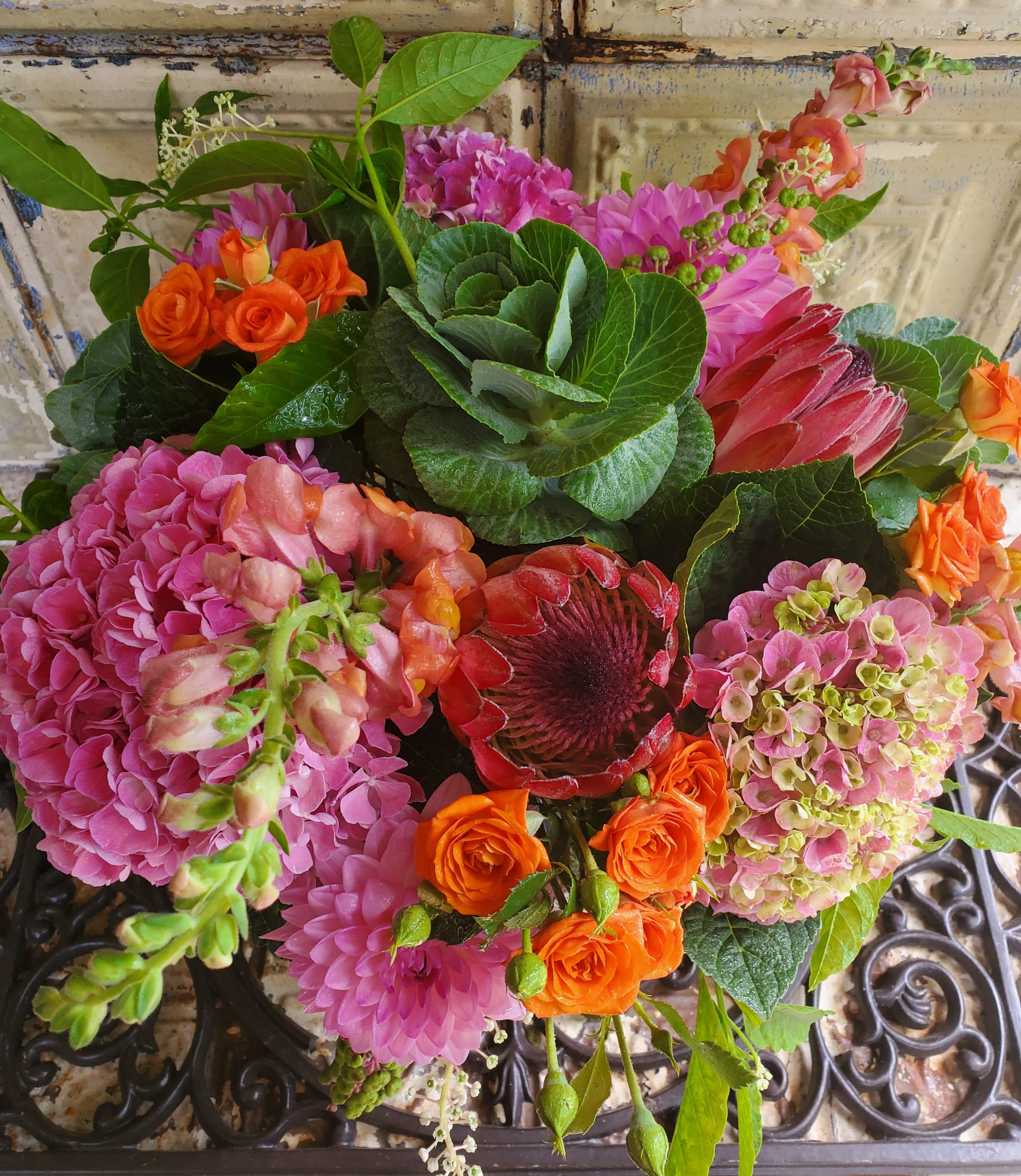 Mixed bouquet with pink hydrangeas, orange roses, and a red protea