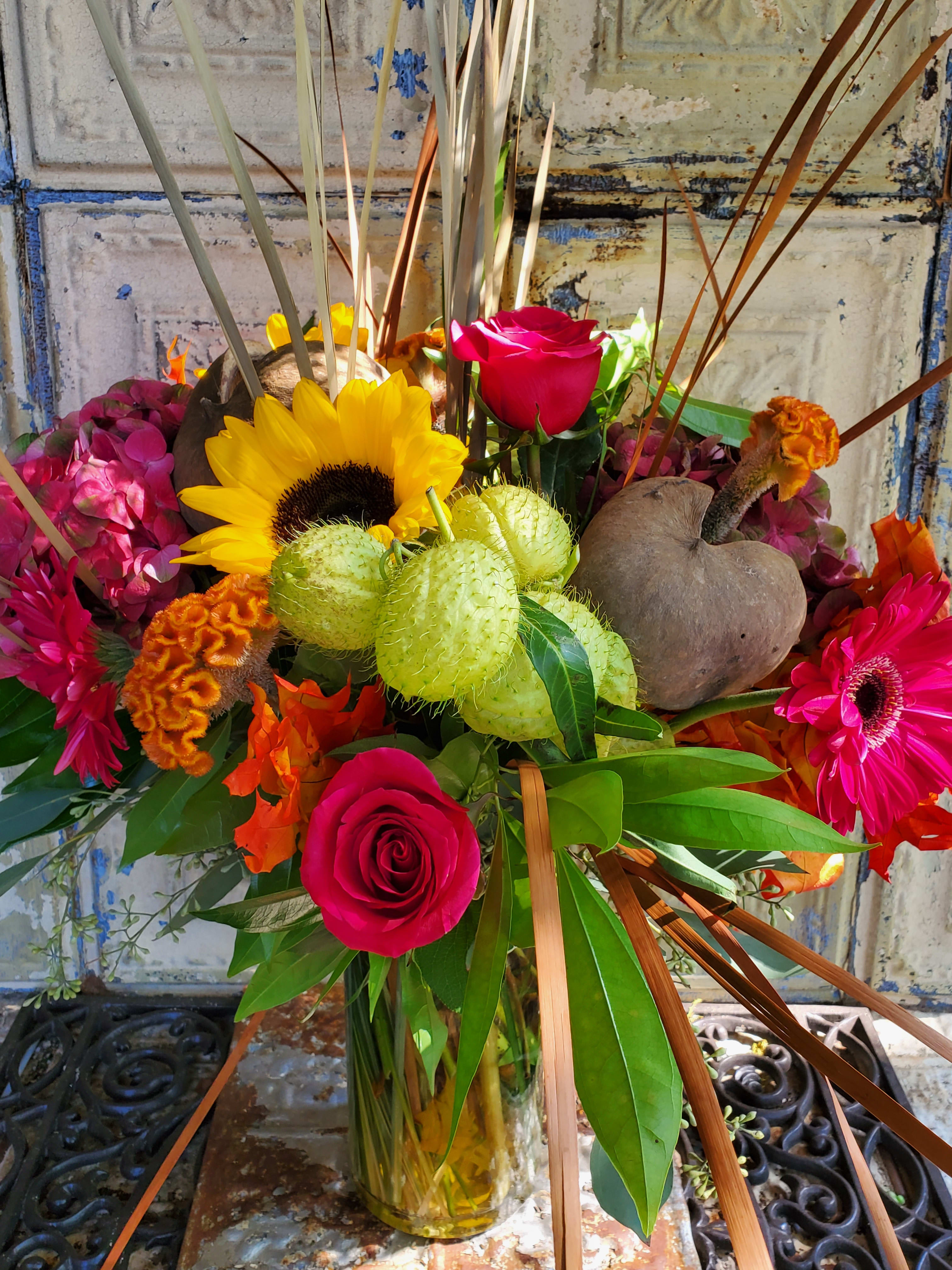 Mixed bouquet with roses, sunflowers, and bright tropical blooms in a glass vase