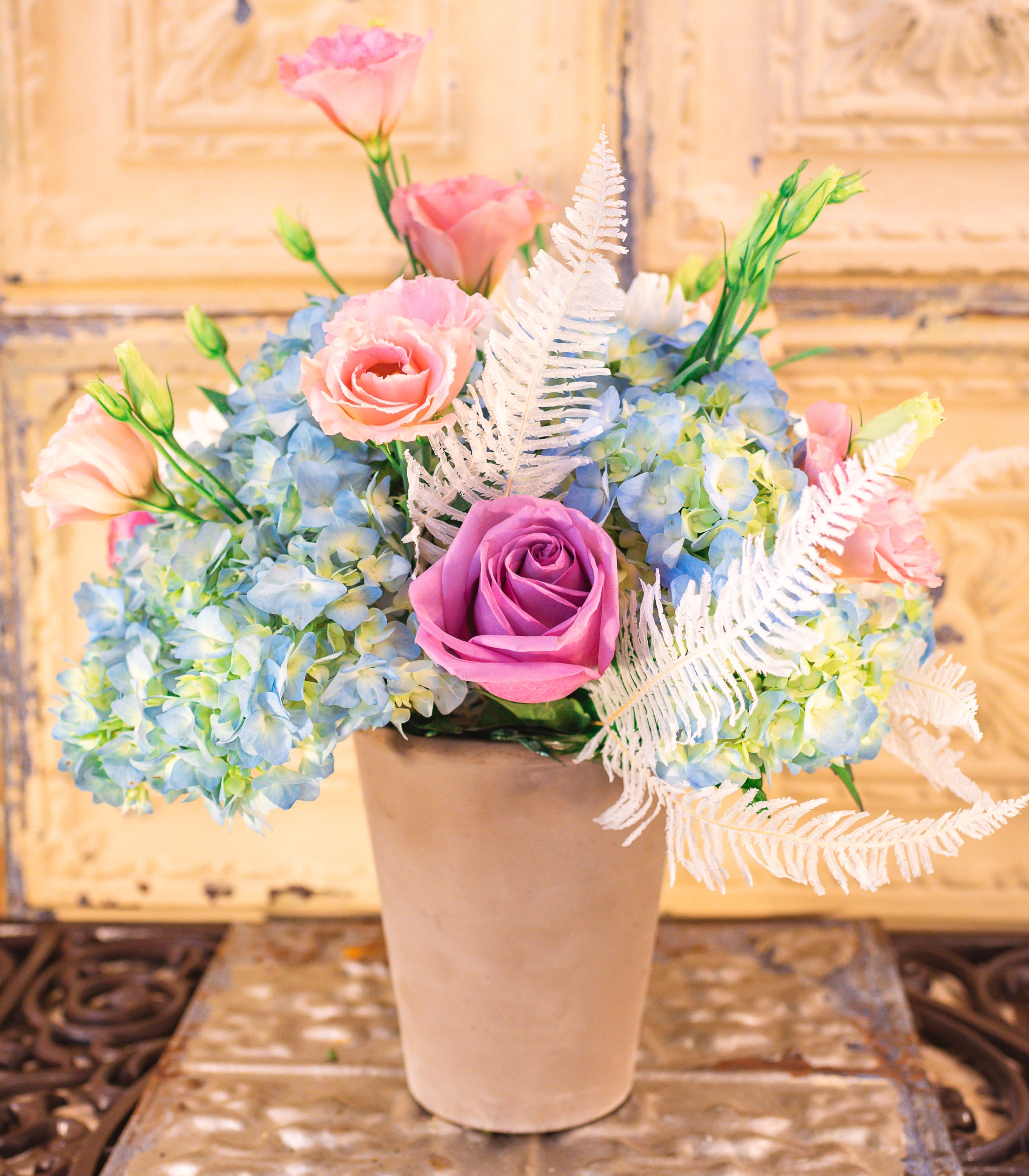 Pink and purple roses with blue hydrangeas in a beige vase
