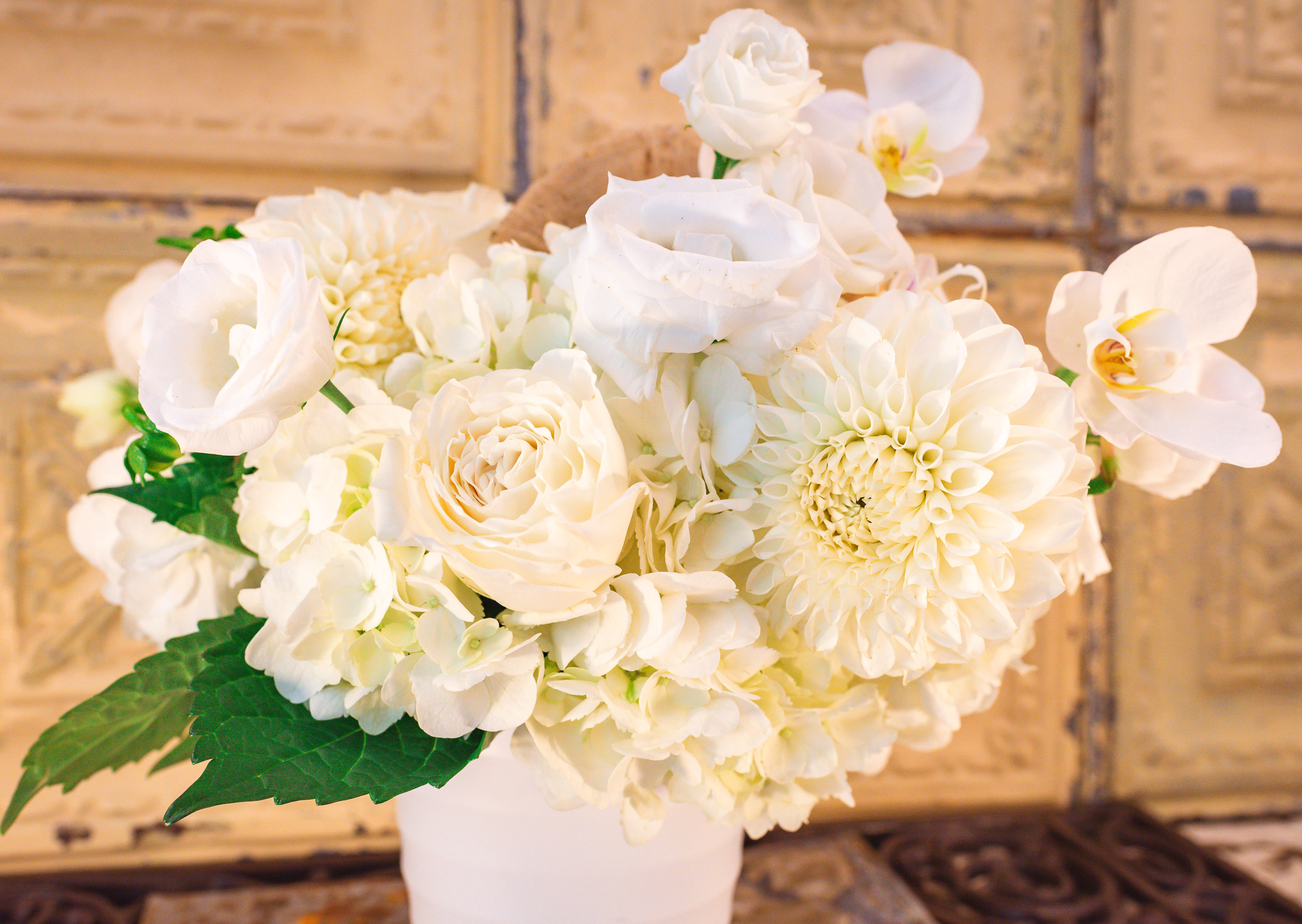 White floral arrangement in a white vase with roses and orchids