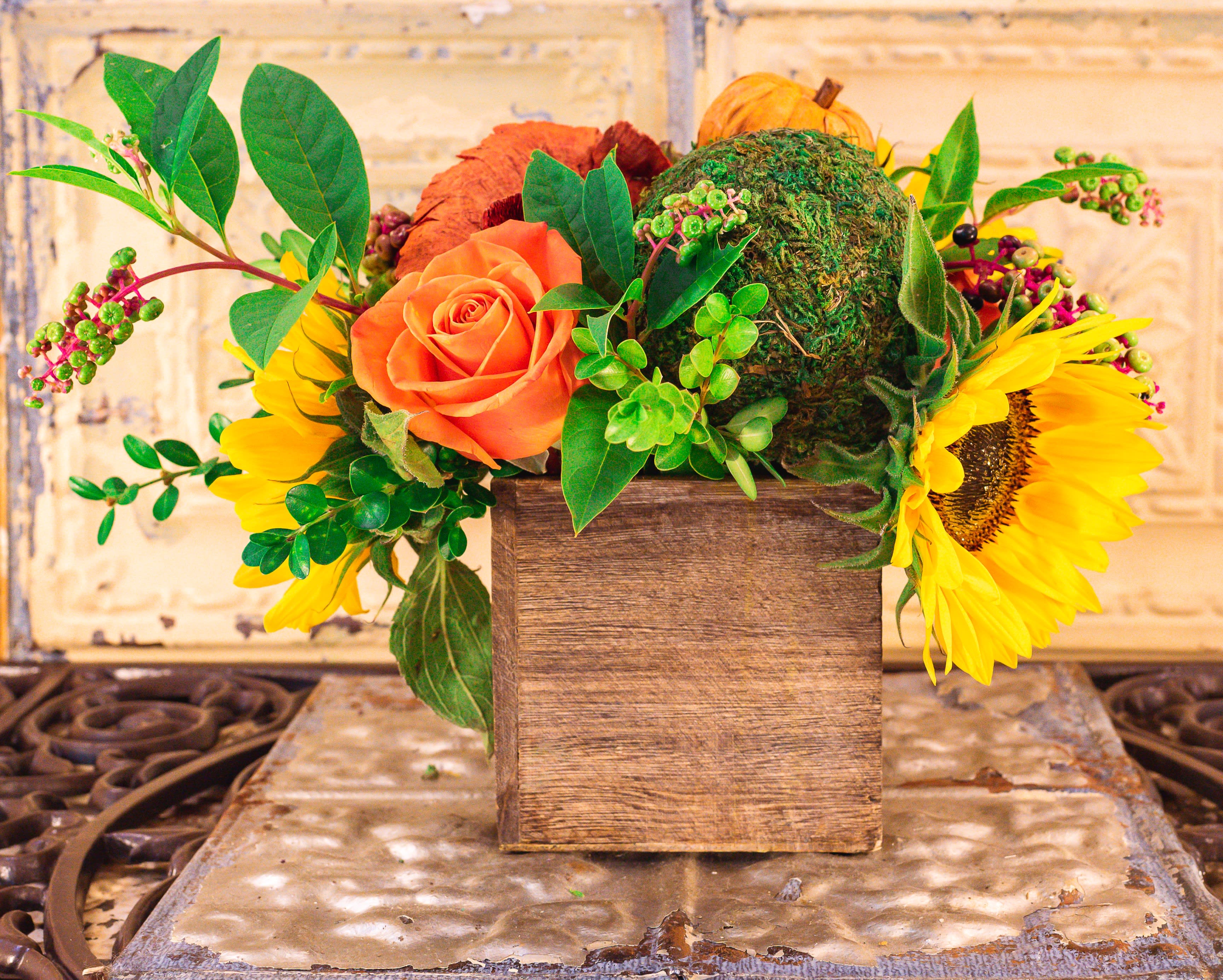 Orange rose and sunflowers in a wooden box with greenery