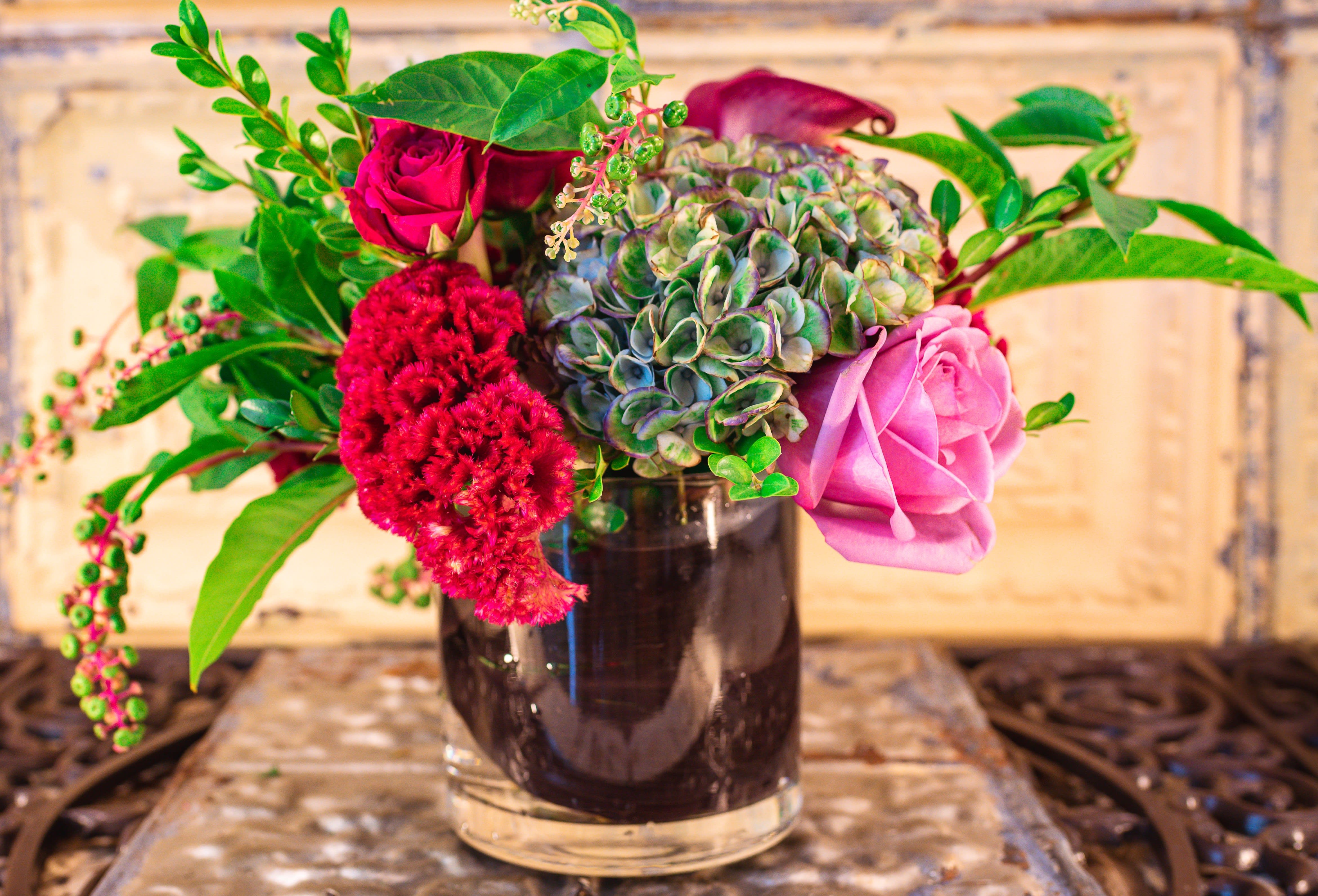 Mixed bouquet in a dark glass vase with pink roses and red blooms