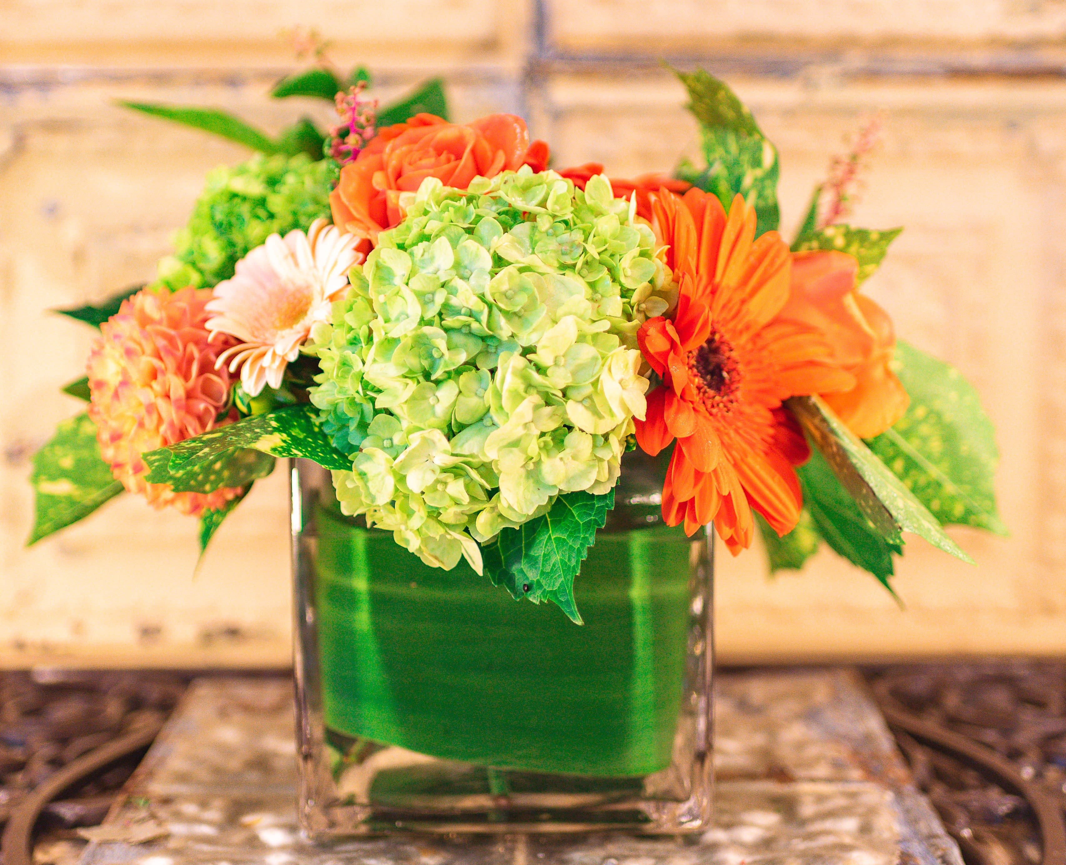 Orange and green floral arrangement in a square glass vase