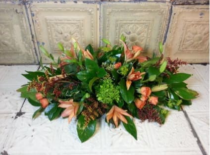 Low floral centerpiece with peach blooms and green foliage