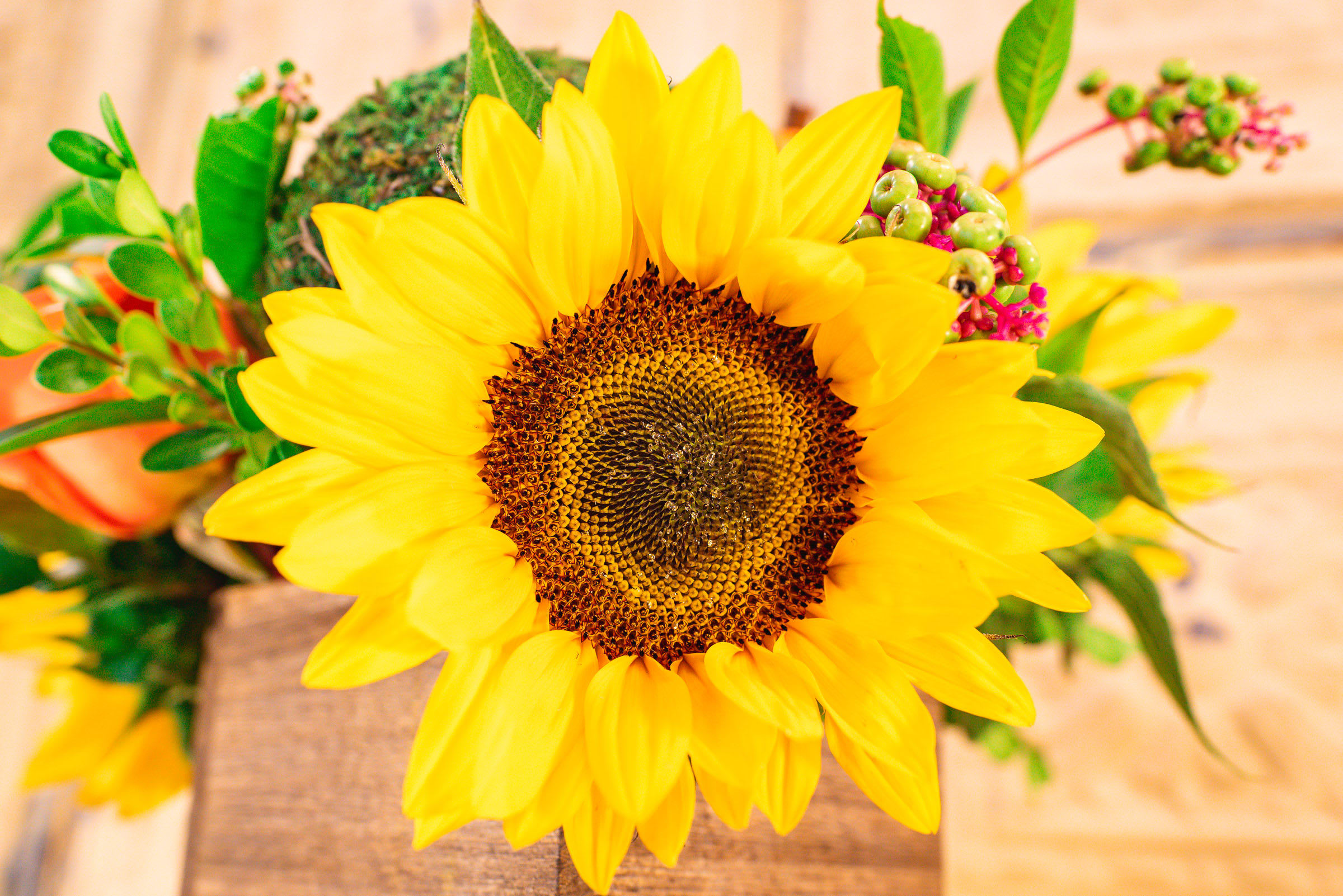Bright yellow sunflower arrangement with green berries and foliage