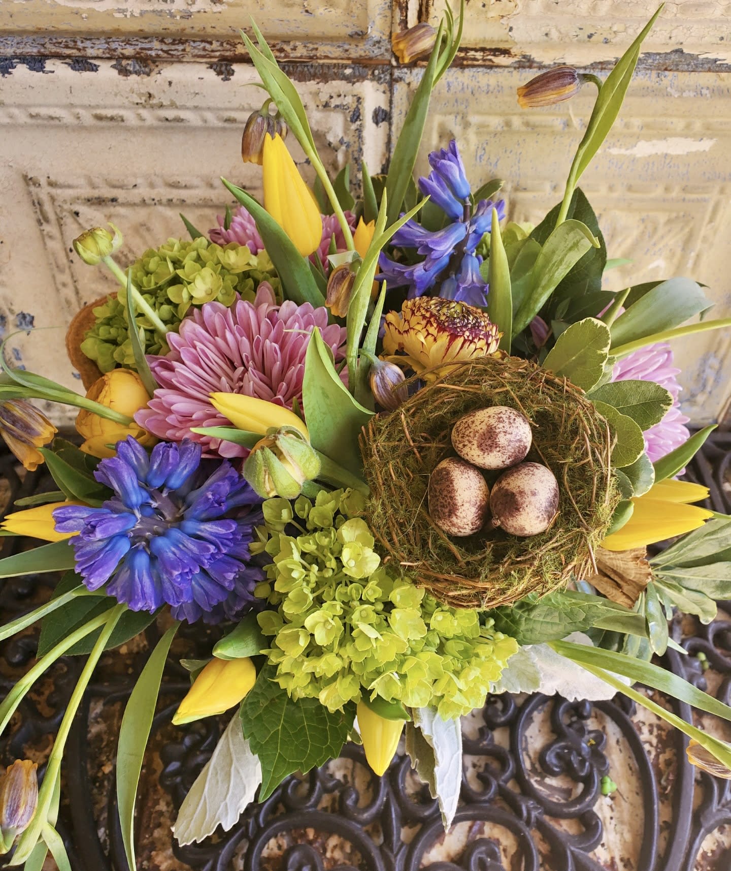 Mixed bouquet with purple and pink flowers, yellow tulips, and a bird nest centerpiece