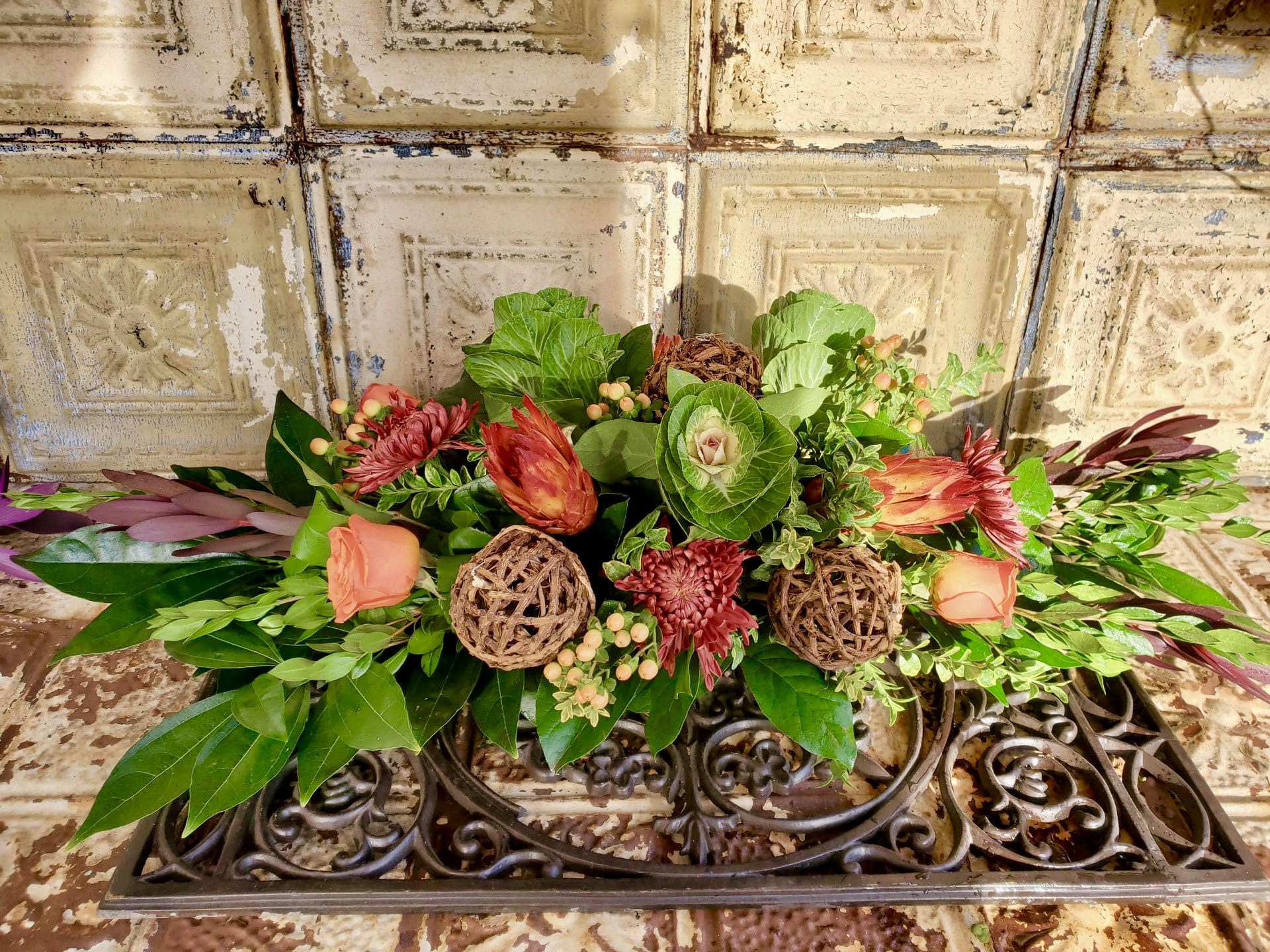 Low floral arrangement with peach roses and red blooms on a decorative metal stand