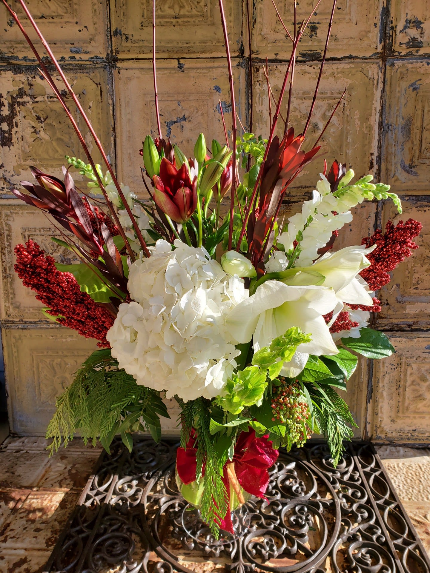Tall floral arrangement with white hydrangeas, lilies, and red accents in a vase