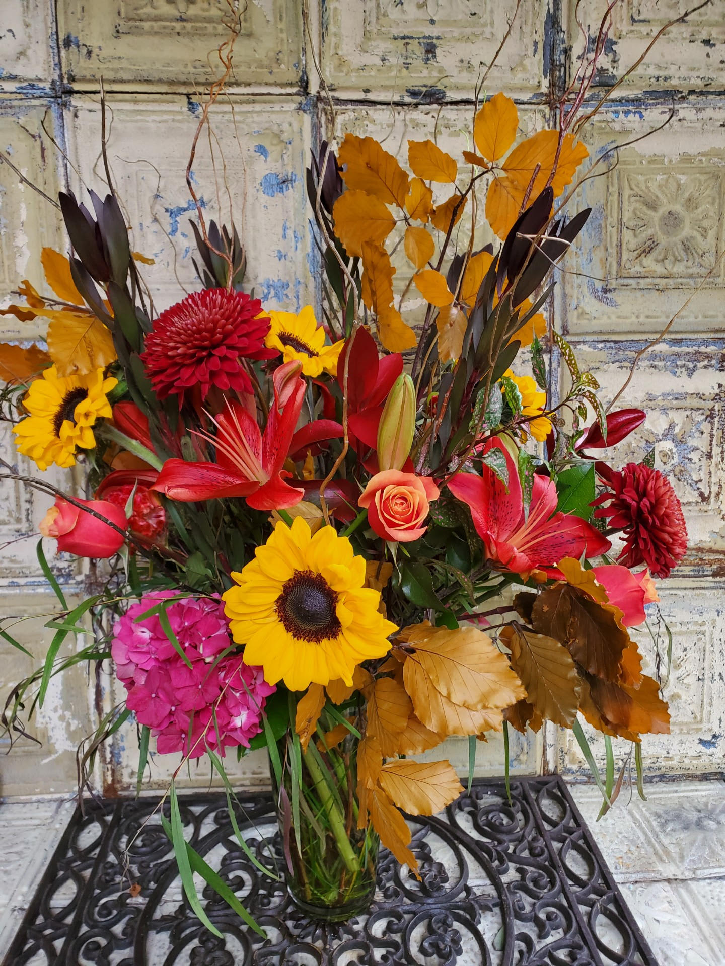 Autumn bouquet with sunflowers, red lilies, and orange leaves in a glass vase