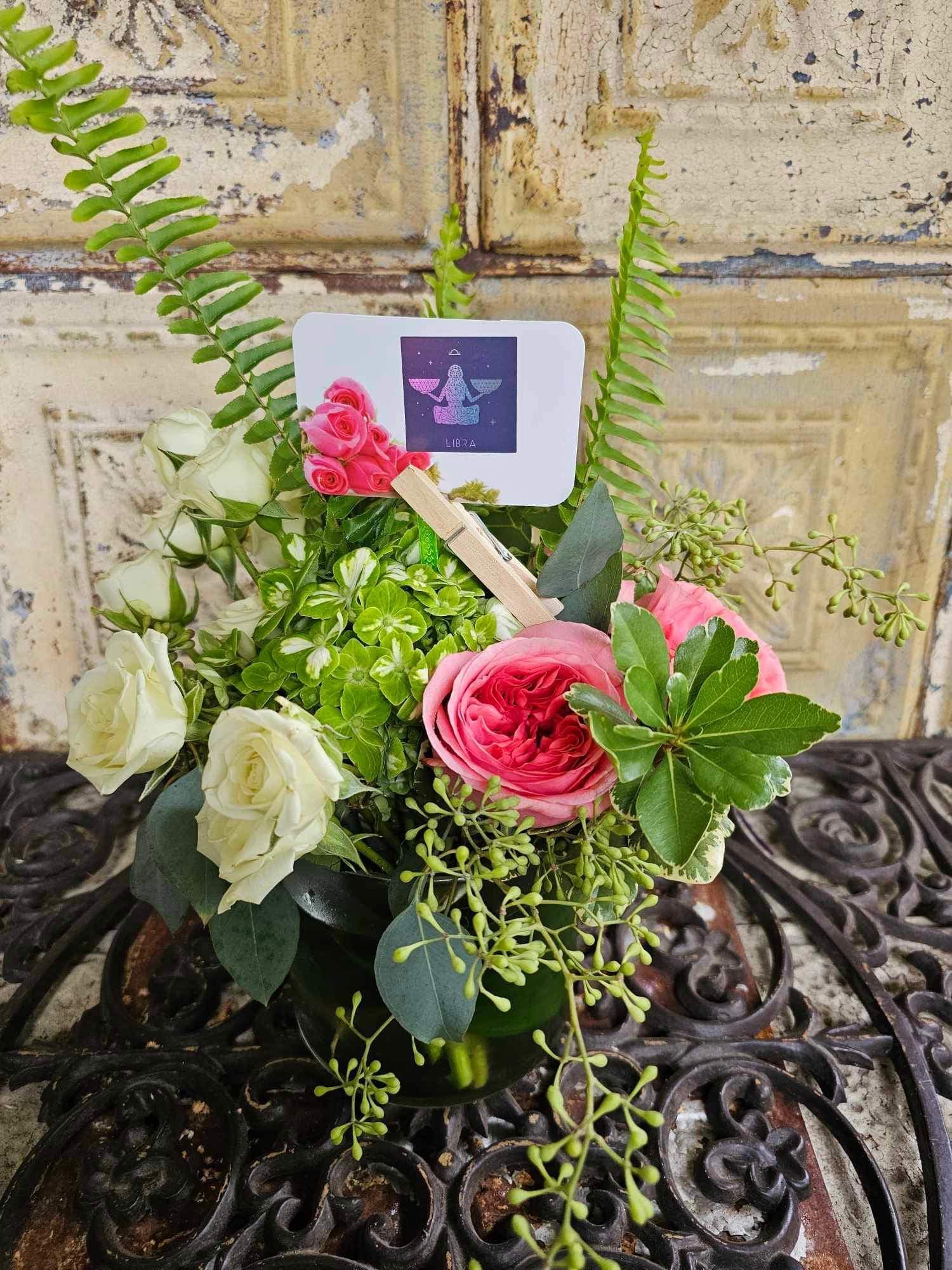 Pink and white roses arranged in a small vase with a Libra card