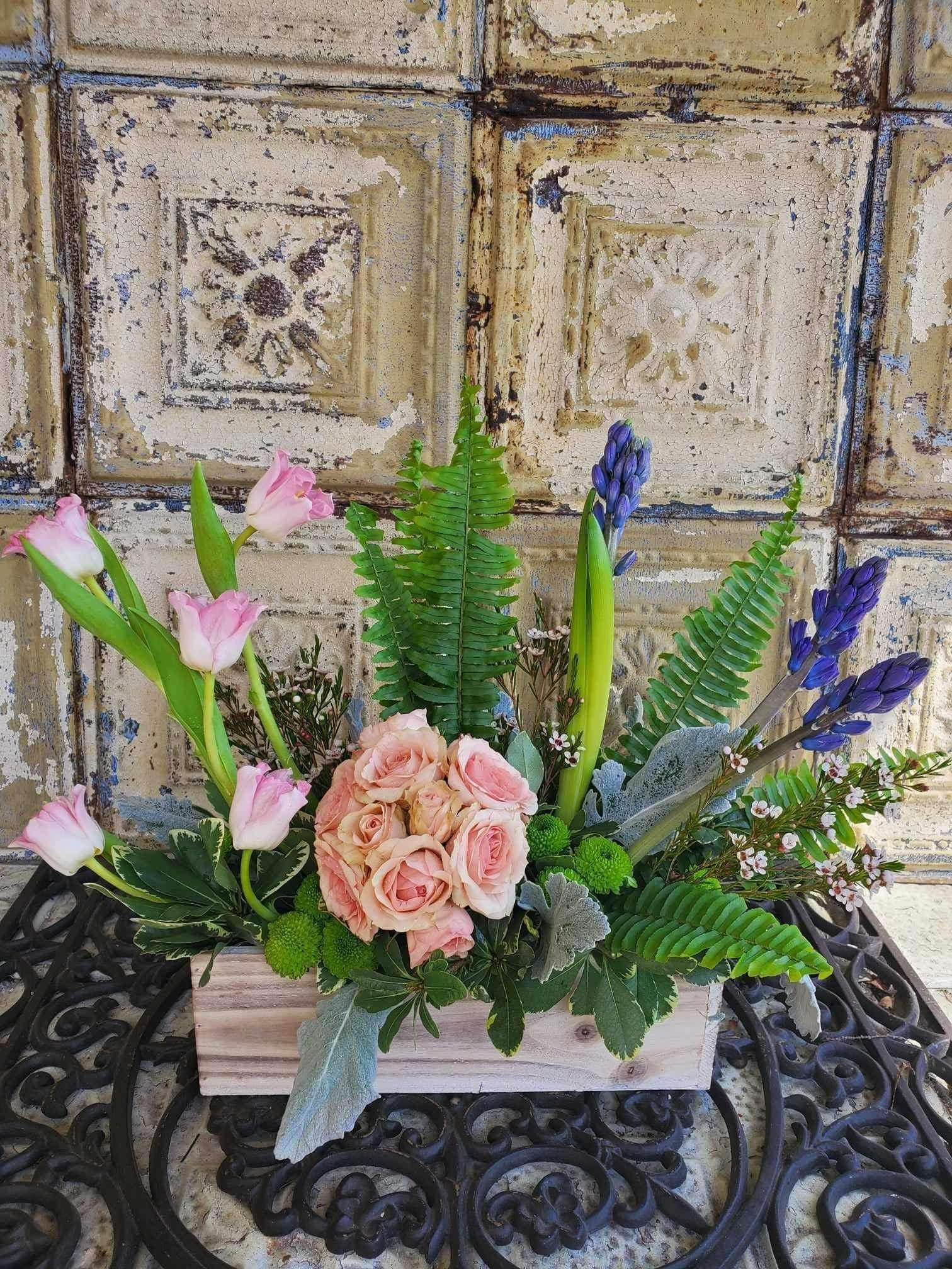Pink roses and tulips arranged in a wooden box with purple blooms