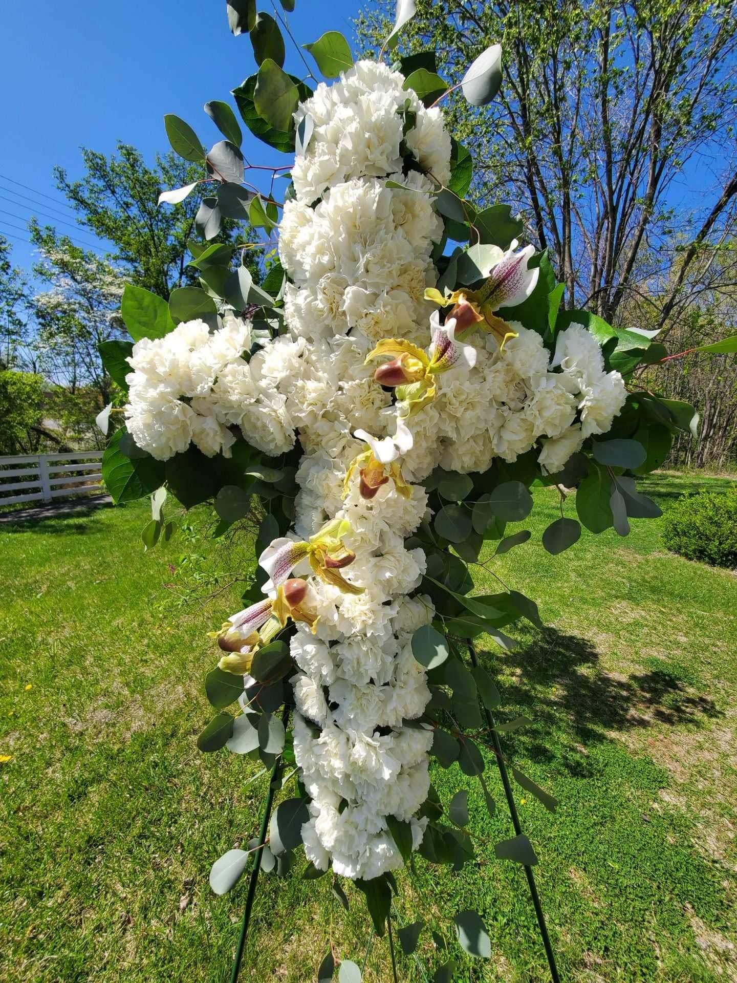 Large white floral cross on an outdoor stand with green foliage