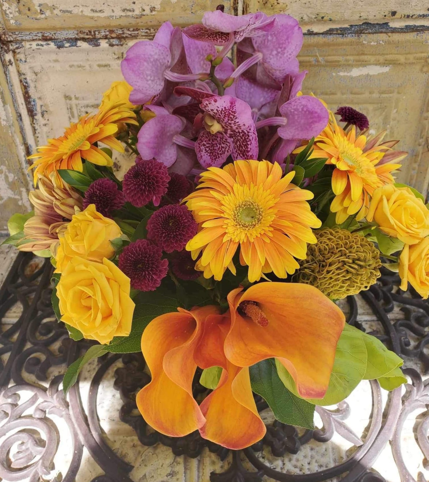 Bouquet with purple orchids, yellow roses, orange calla lilies, and mixed daisies