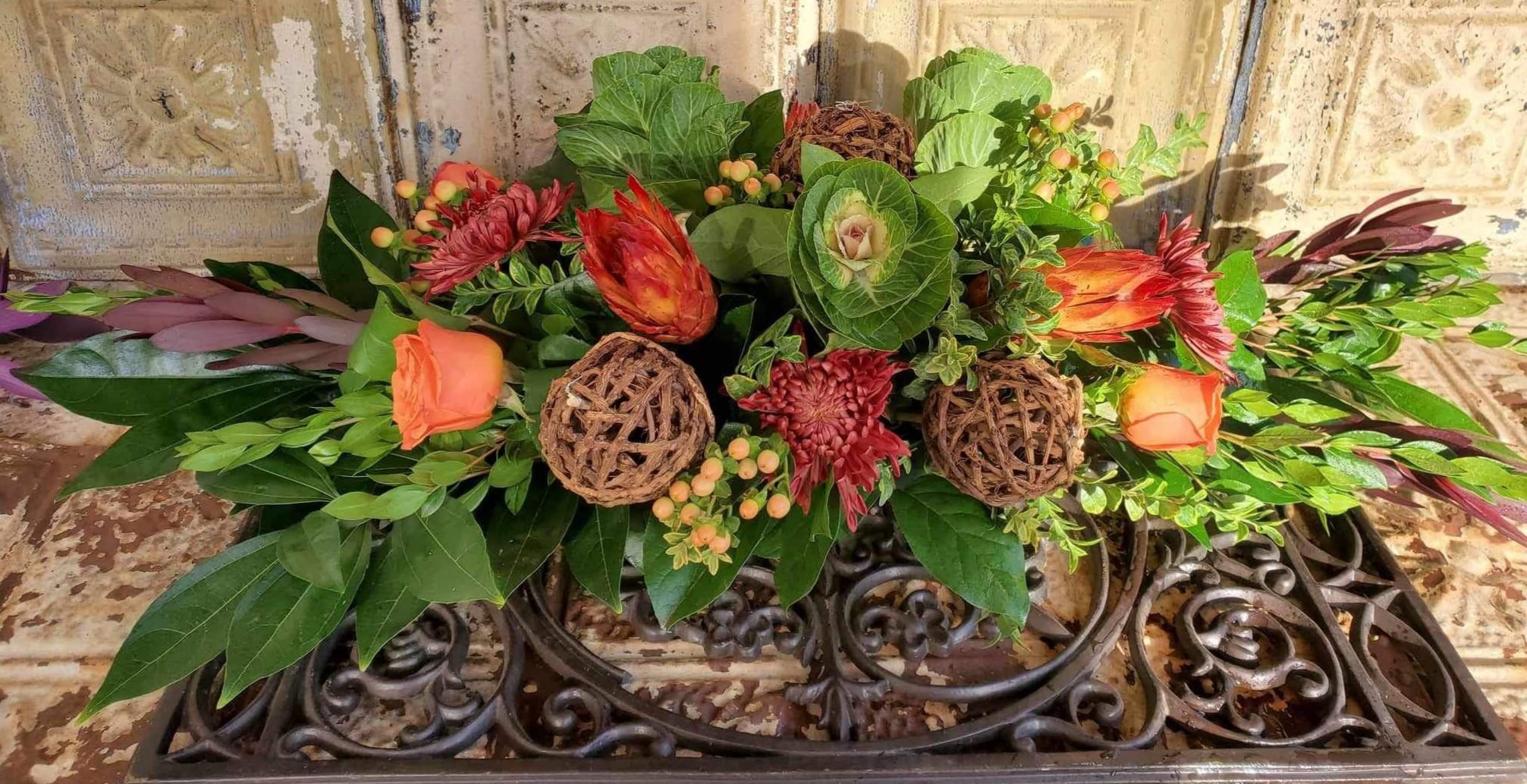 Low floral arrangement with orange roses and red blooms in a decorative container