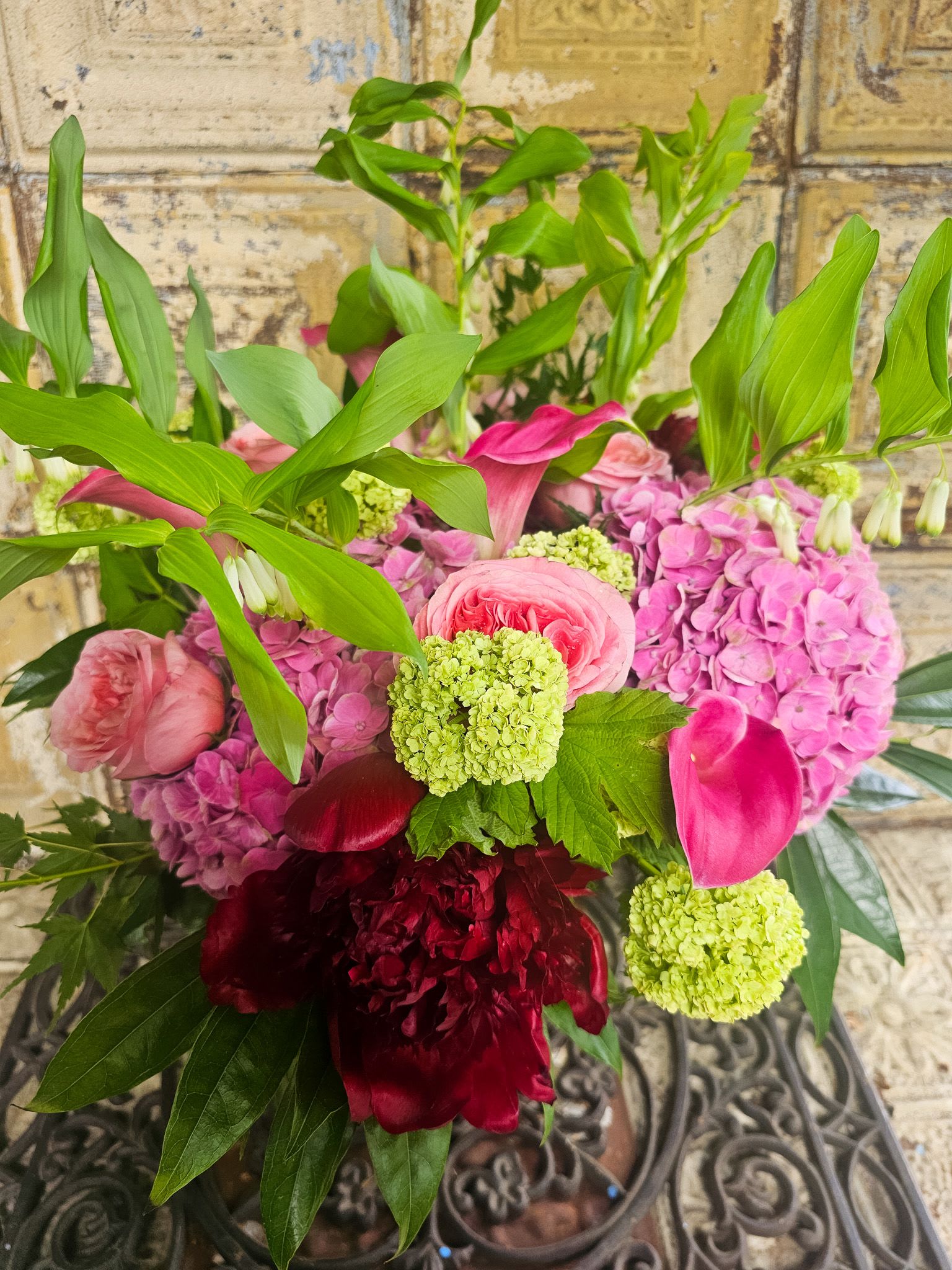 Pink and burgundy floral bouquet with green tropical foliage