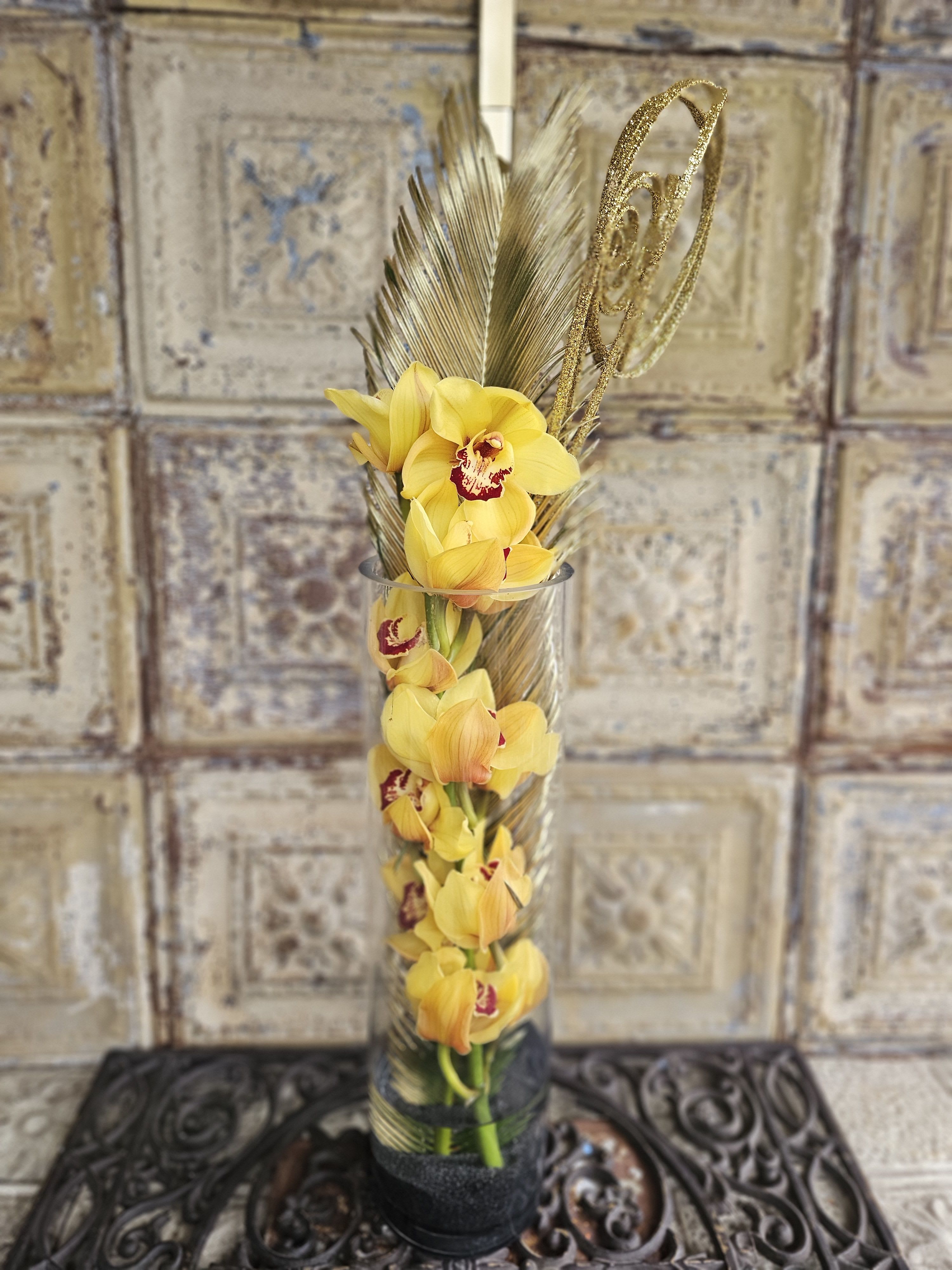 Yellow orchids in a tall glass vase with decorative feathers