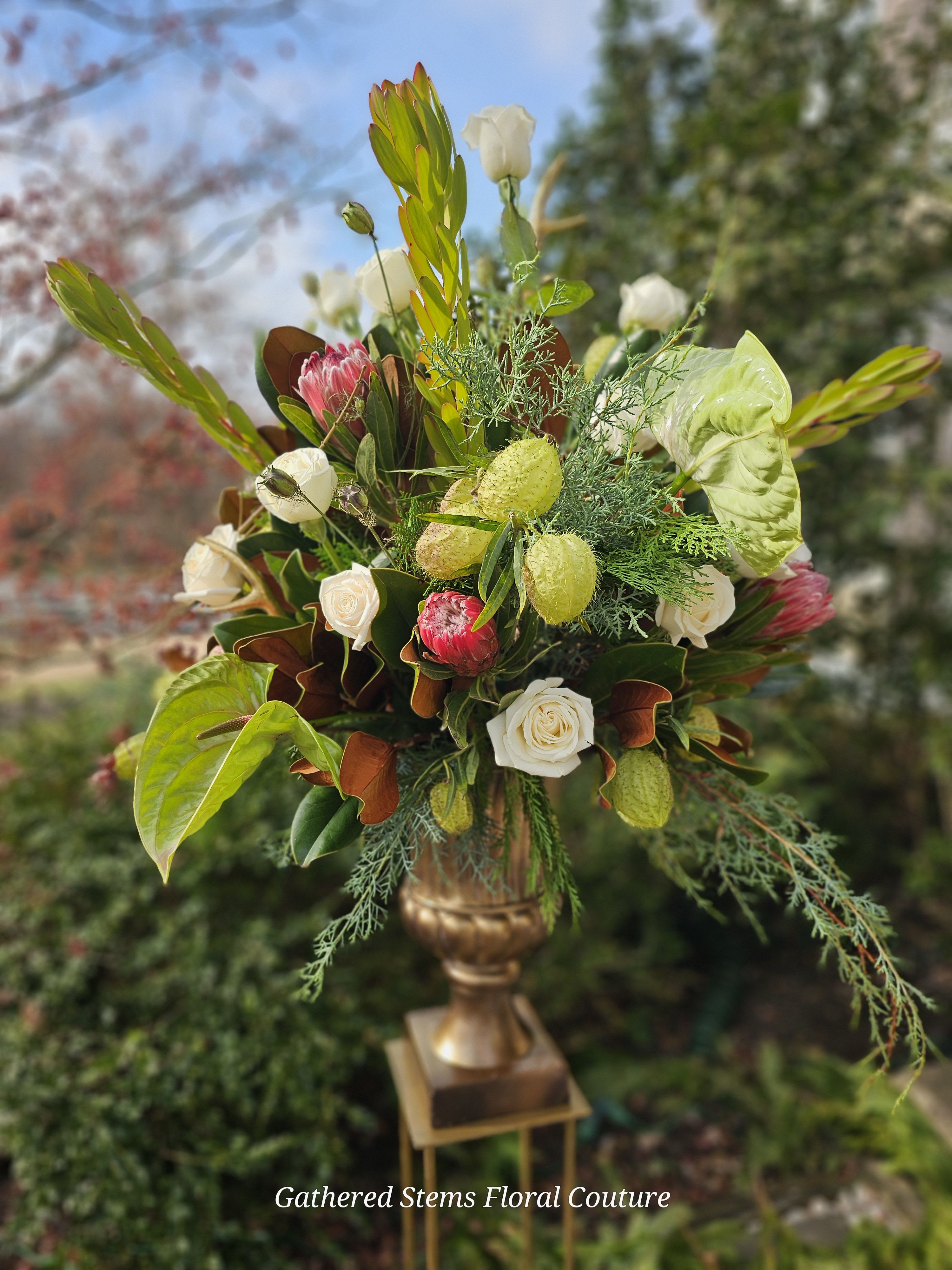 Tall floral arrangement with white roses and pink protea in a gold vase